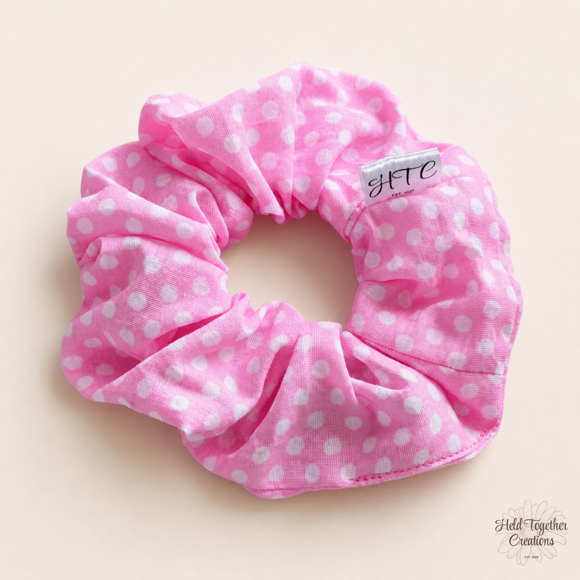 Pink handmade scrunchie with white polka dots on a warm neutral background.
