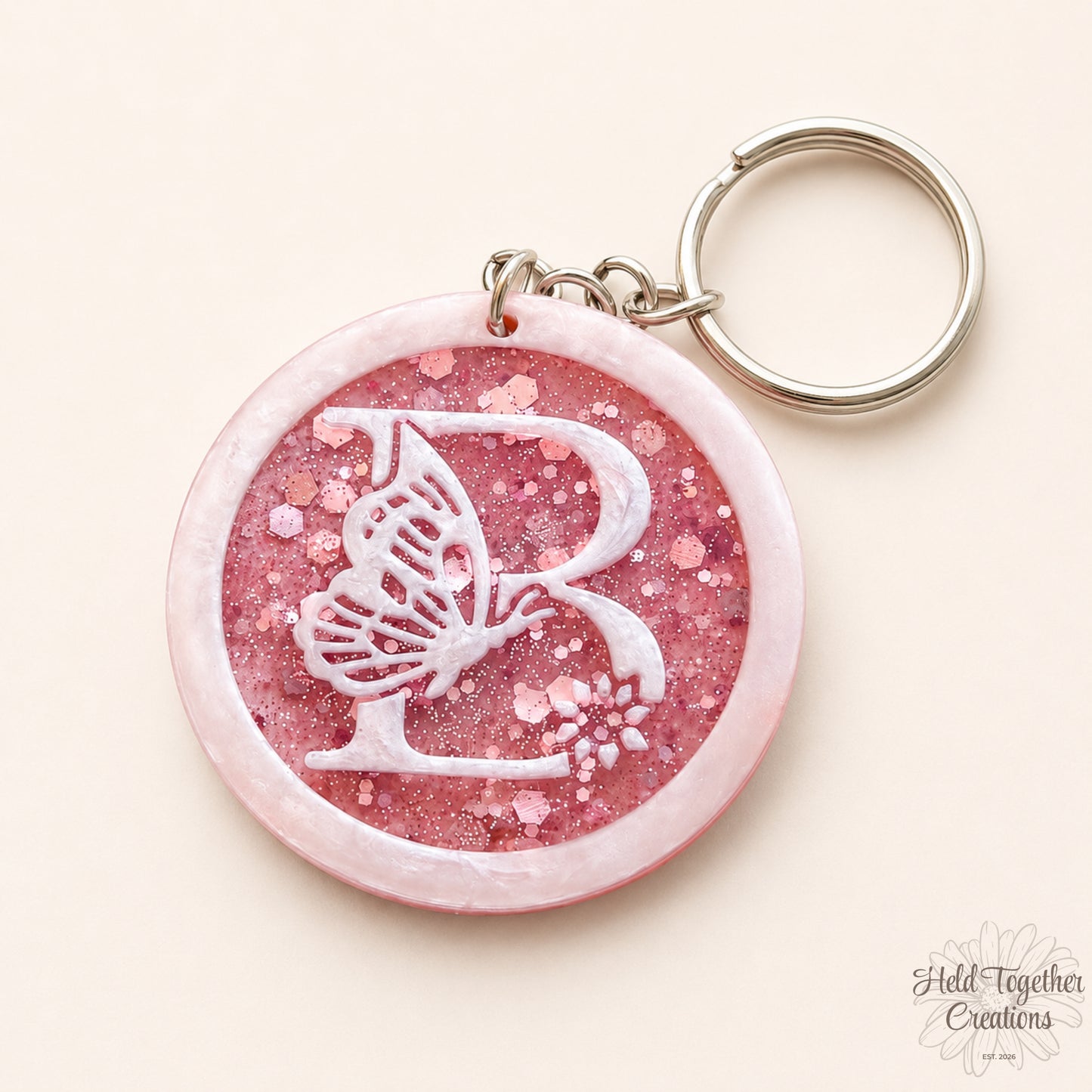 Pink glittery keychain with butterfly design and 'R' letter on a white background