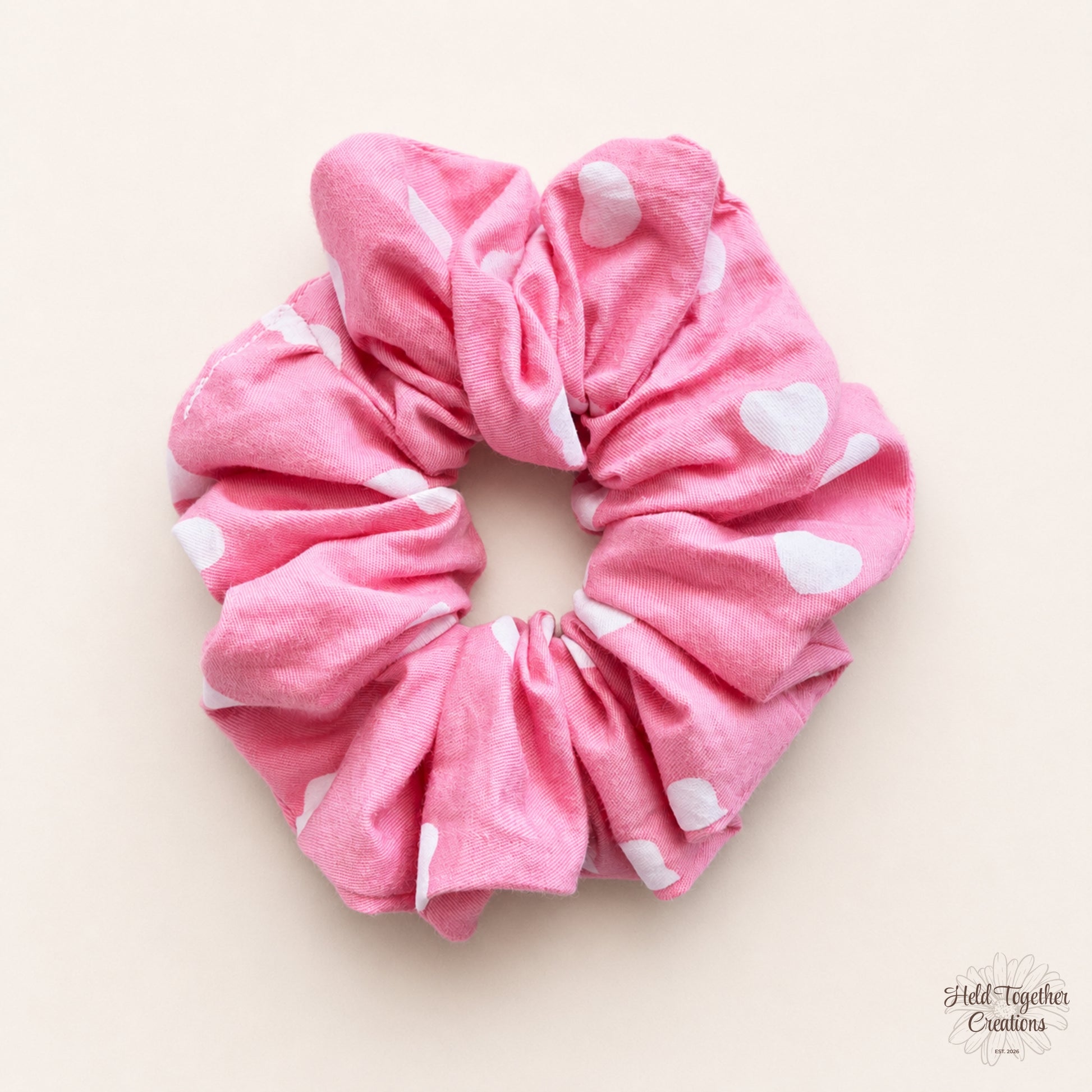 Candy Hearts Scrunchie in pink fabric with white heart print on a warm neutral background.