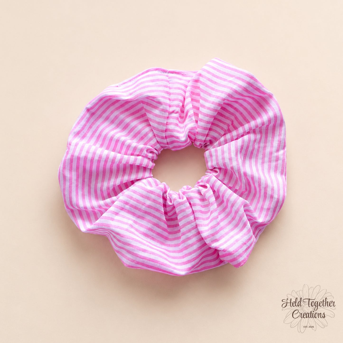 Handmade pink and white candy stripe fabric scrunchie on a soft neutral background.