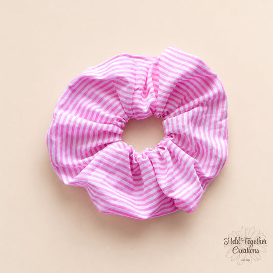 Handmade pink and white candy stripe fabric scrunchie on a soft neutral background.