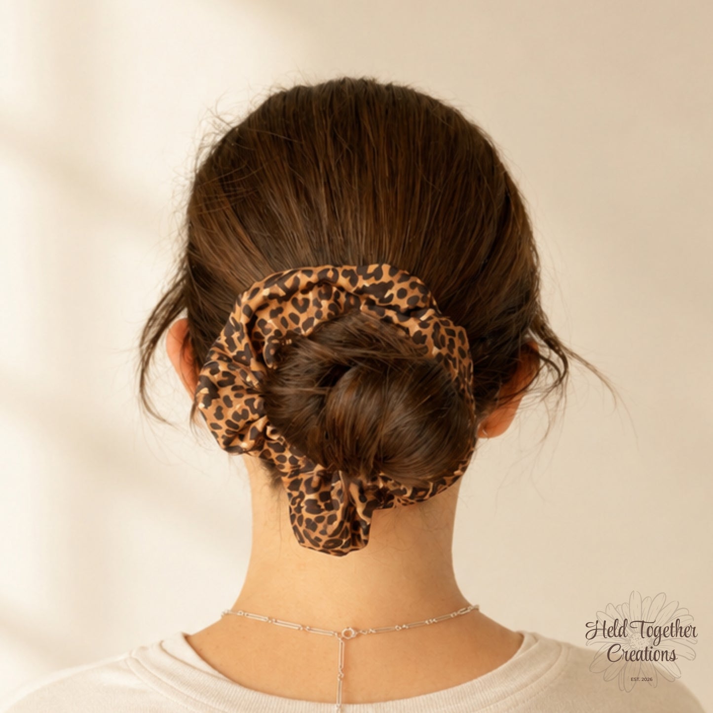 Cocoa Prowl Scrunchie styled in a low bun, showing the brown leopard print fabric against dark hair.