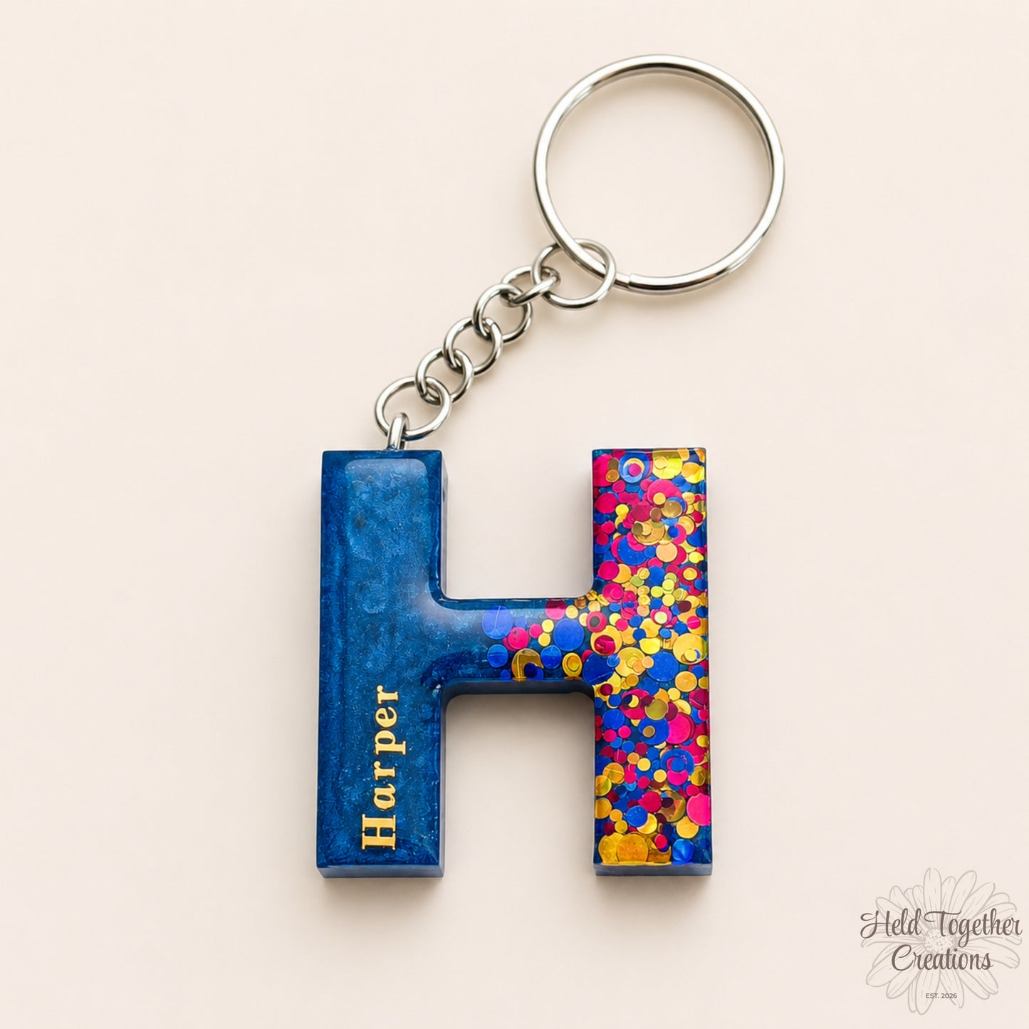Keychain with a blue letter 'H' and colorful confetti design on a beige background