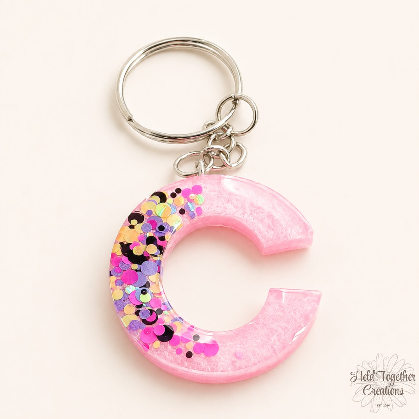 Pink crescent-shaped keychain with colorful confetti on a white background