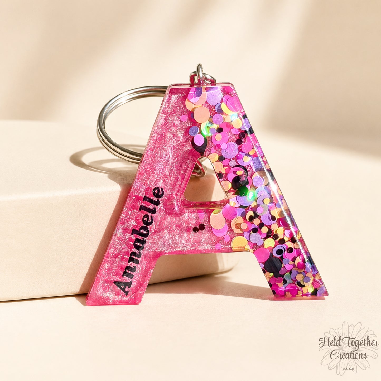 Colourful letter-shaped keychains with confetti details on a marble background - in sun