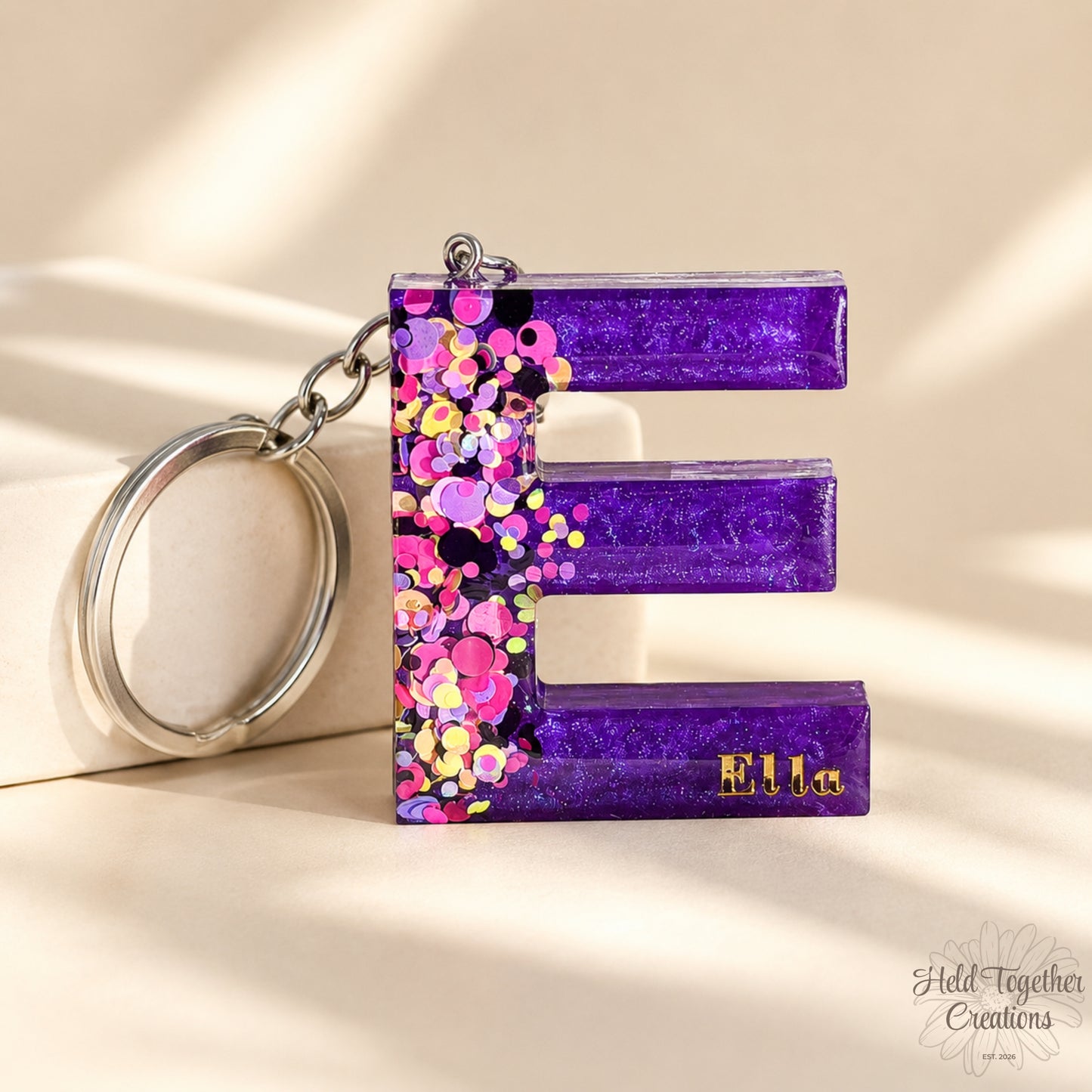 Colourful letter-shaped keychains with confetti details on a marble background - in sun