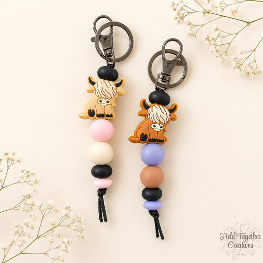 Handmade highland cow silicone bead keyrings with soft silicone beads and black keyring hardware on a neutral background.