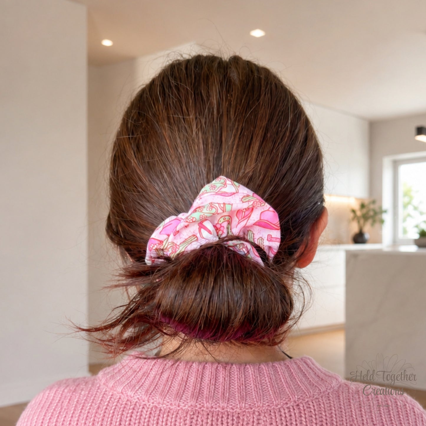 Pink Cowgirl Crush handmade scrunchie worn in a low bun, featuring a pink western print with cowgirl boots, hats, cacti and floral details.