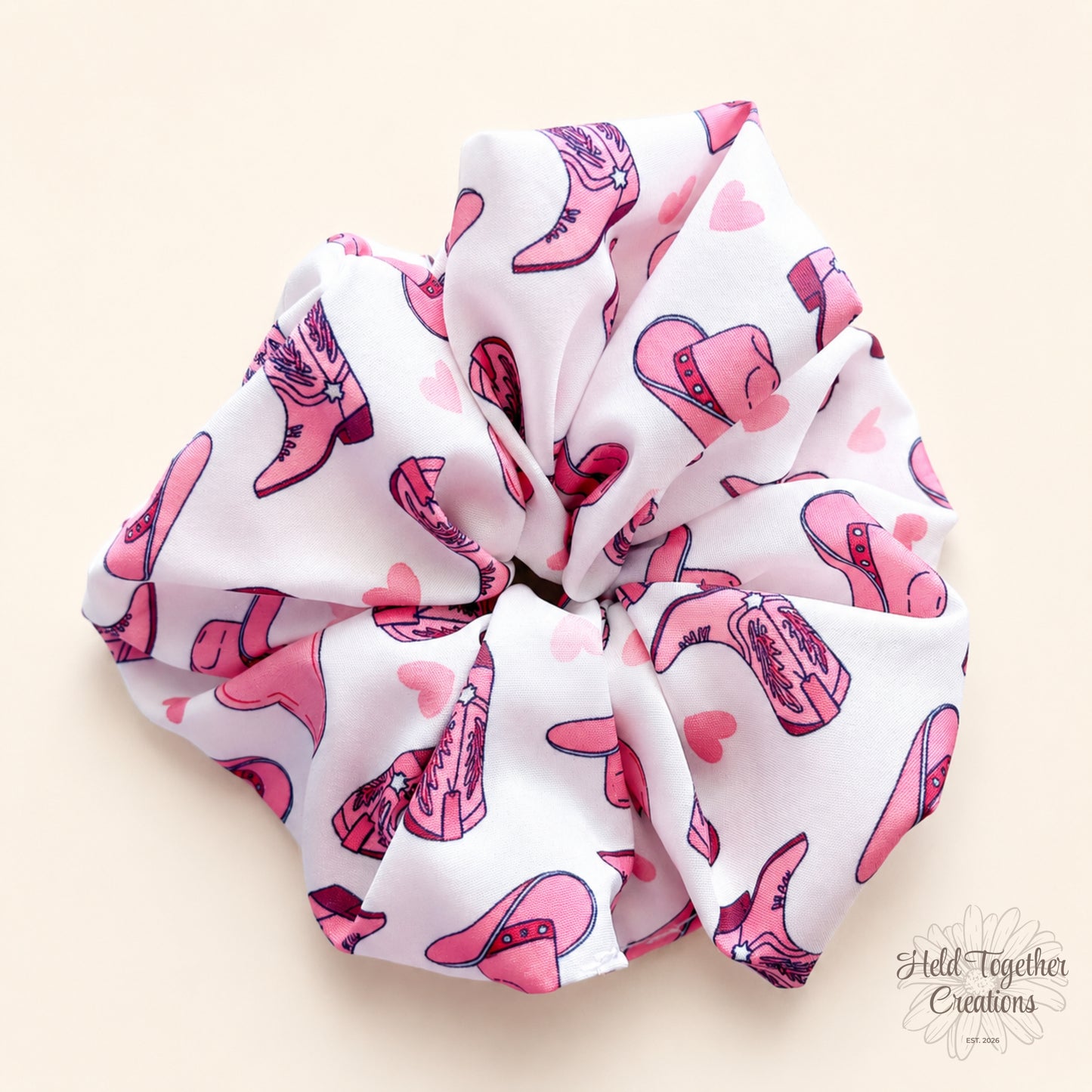White Cowgirl Crush handmade scrunchie on a warm ivory background, featuring pink cowgirl boots, hats and heart details.