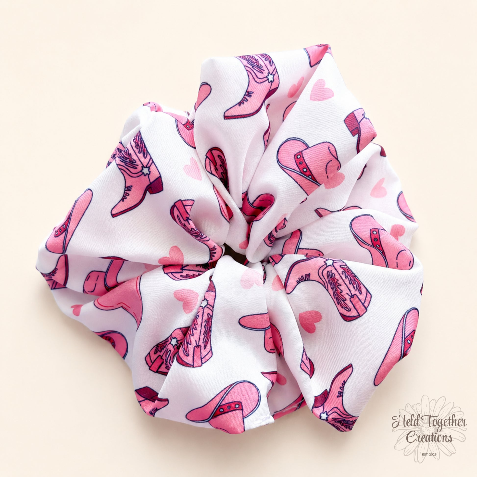 White Cowgirl Crush handmade scrunchie on a warm ivory background, featuring pink cowgirl boots, hats and heart details.