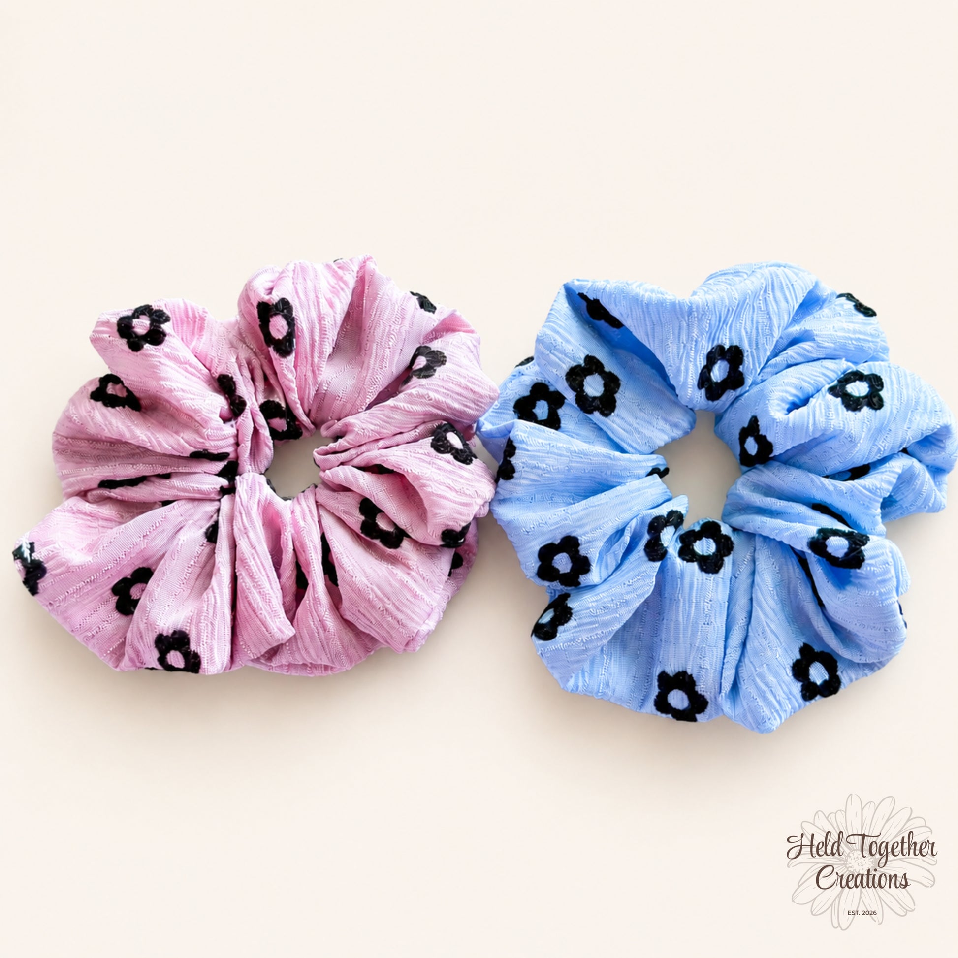 Pink and blue Daisy Charm Scrunchies side by side on warm ivory background
