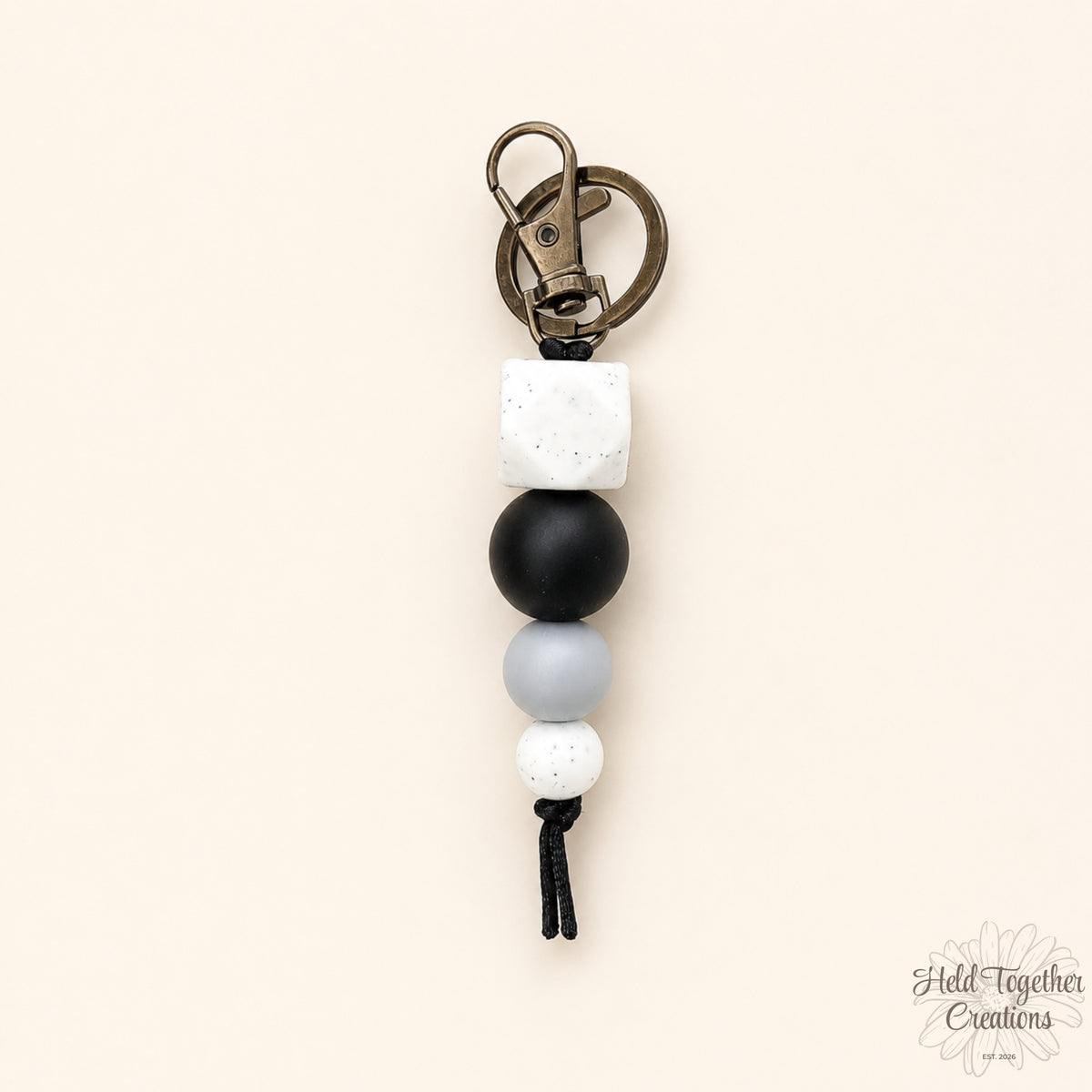 Dark & Stormy silicone bead keyring with white speckled hex bead, black bead, grey bead and small white speckled bead on a warm ivory background.