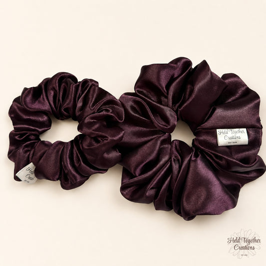 Small and large deep plum satin scrunchies shown together on a neutral background