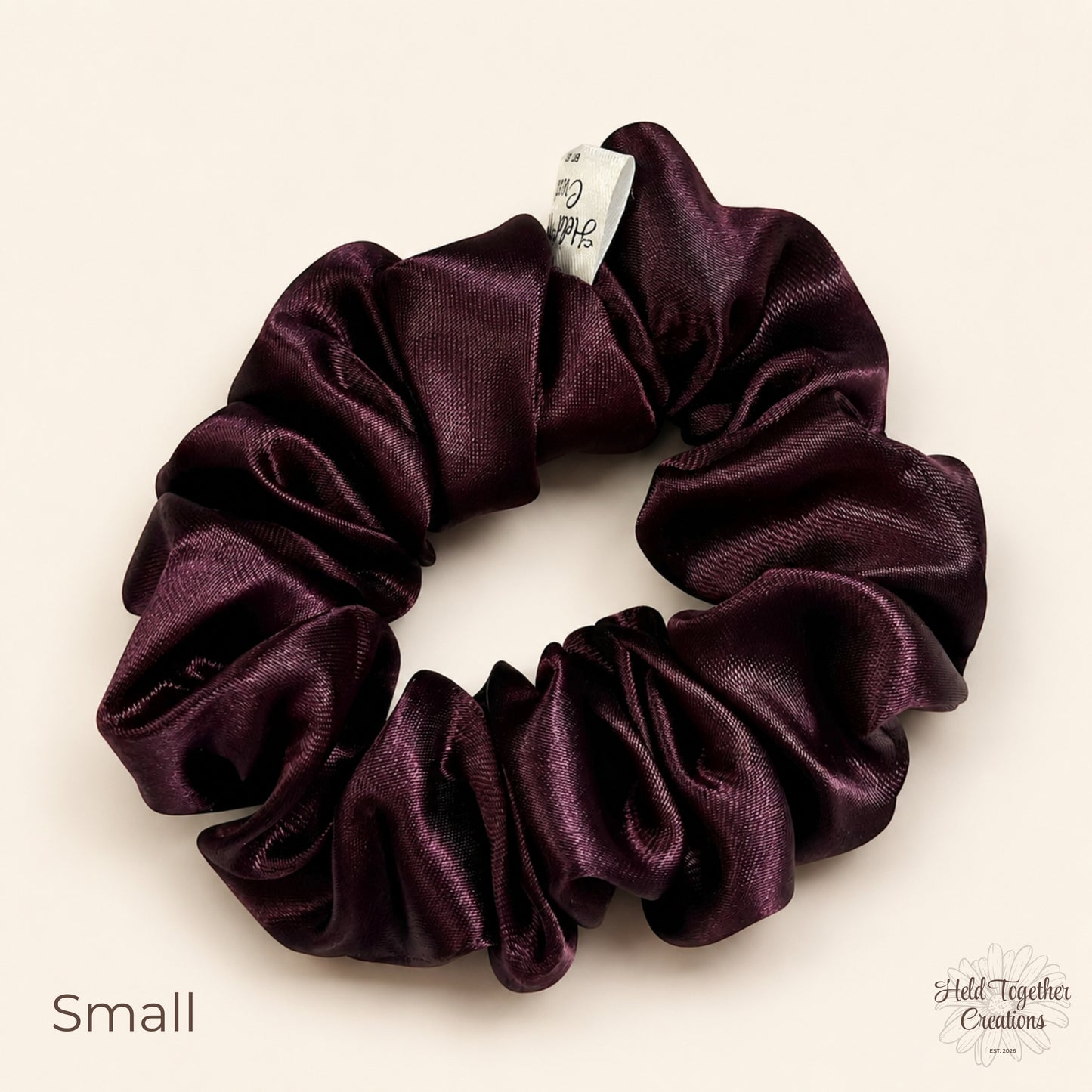 Small deep plum satin scrunchie on a warm ivory background