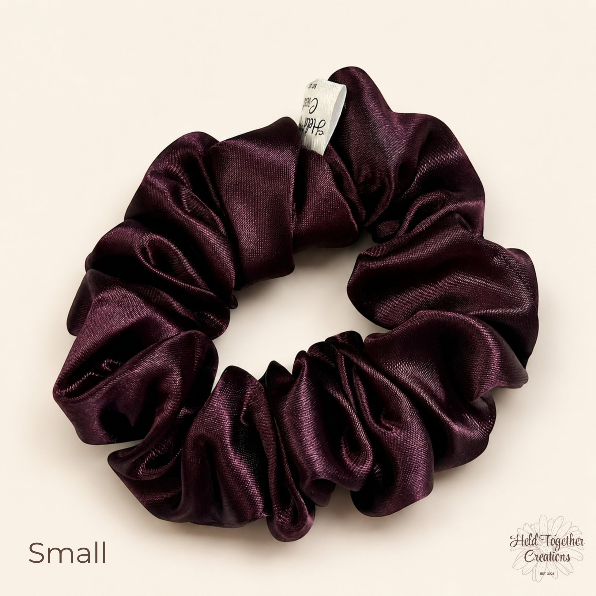 Small deep plum satin scrunchie on a warm ivory background
