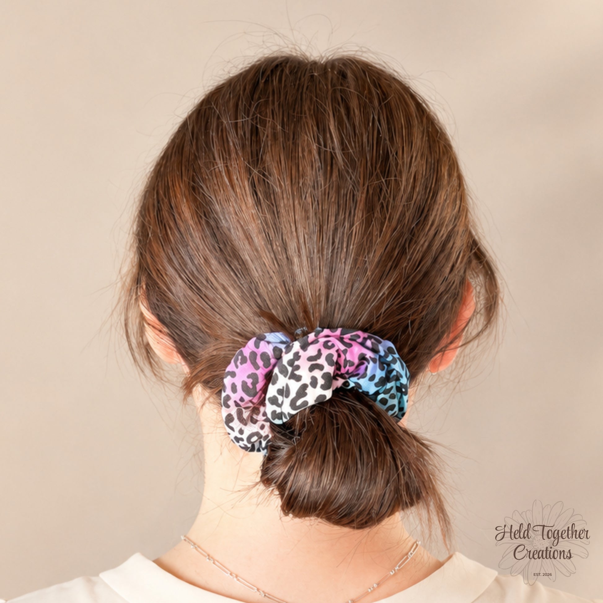 Colourful leopard print handmade scrunchie with pink, blue, purple and black tones on a soft ivory background.