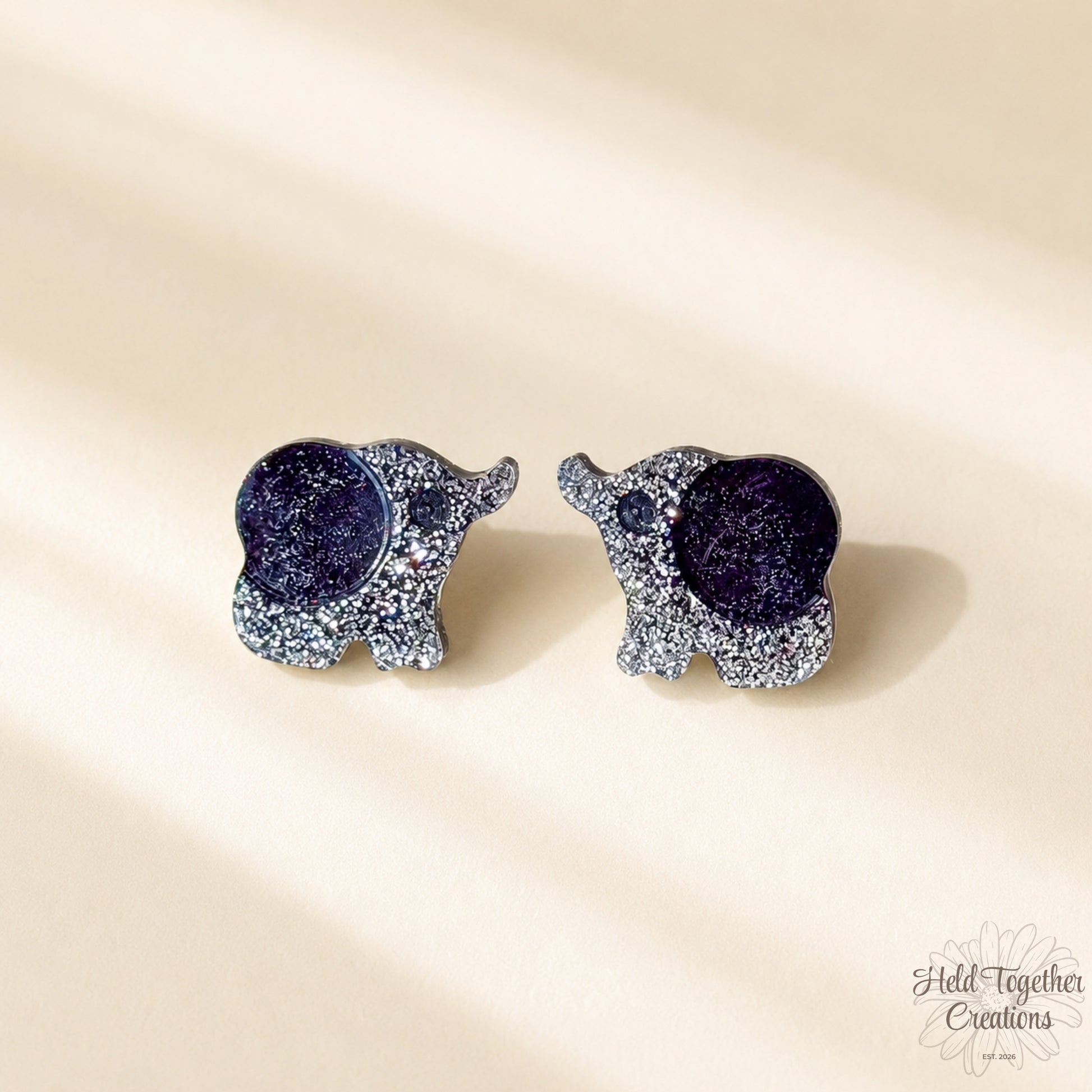 Handmade black and silver speckled elephant resin stud earrings on a soft neutral background.