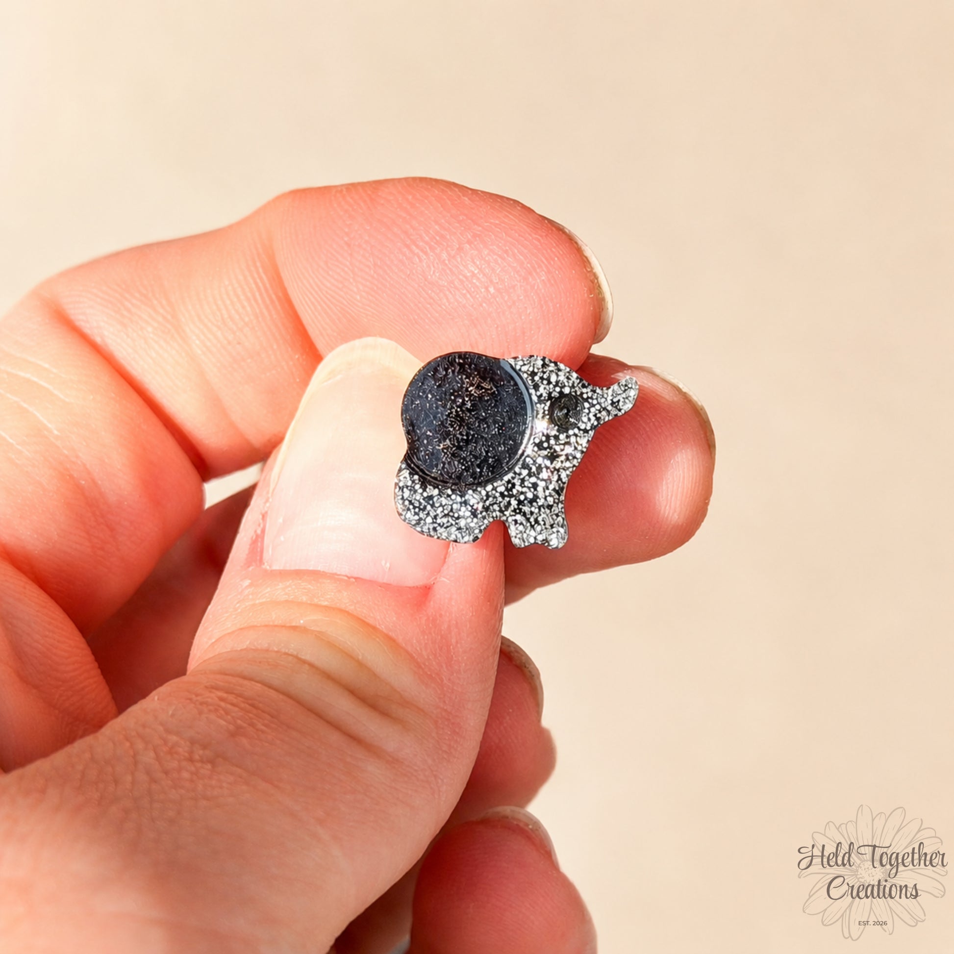 Handmade black and silver speckled elephant resin stud earrings on a soft neutral background.