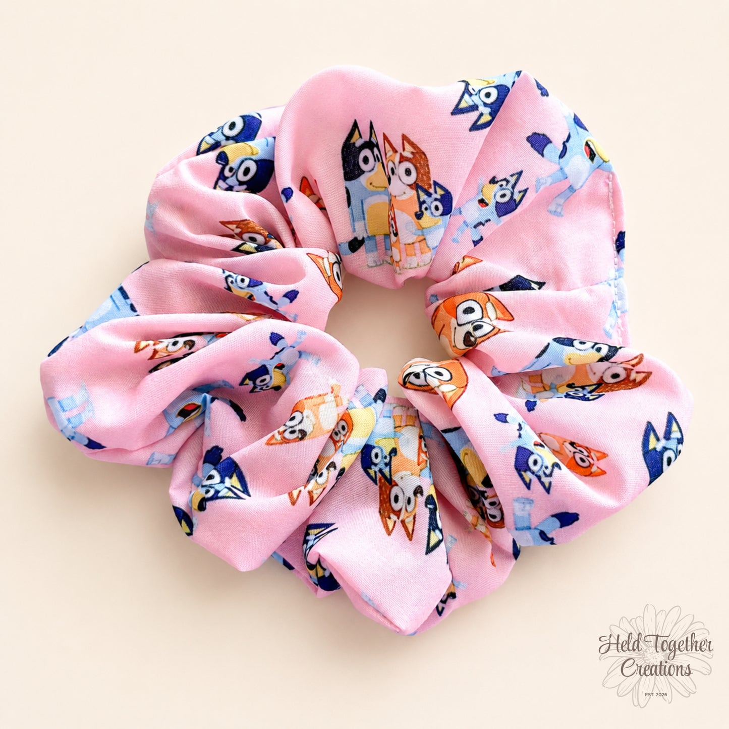 Family Pup handmade scrunchie in pink puppy-print fabric on a warm ivory background with Held Together Creations branding.