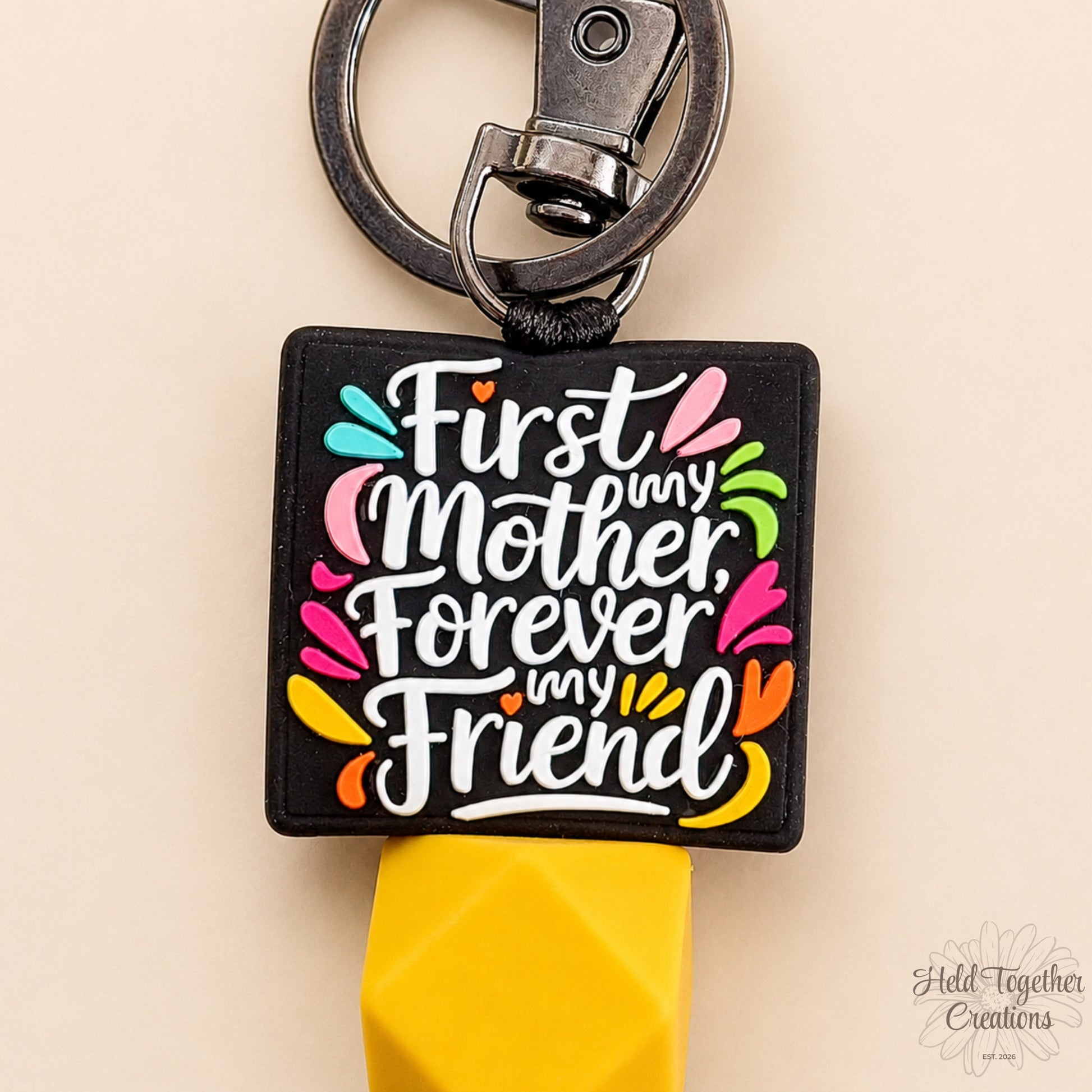 Keychain with colorful text 'First Mother, Forever My Friend' on a beige background