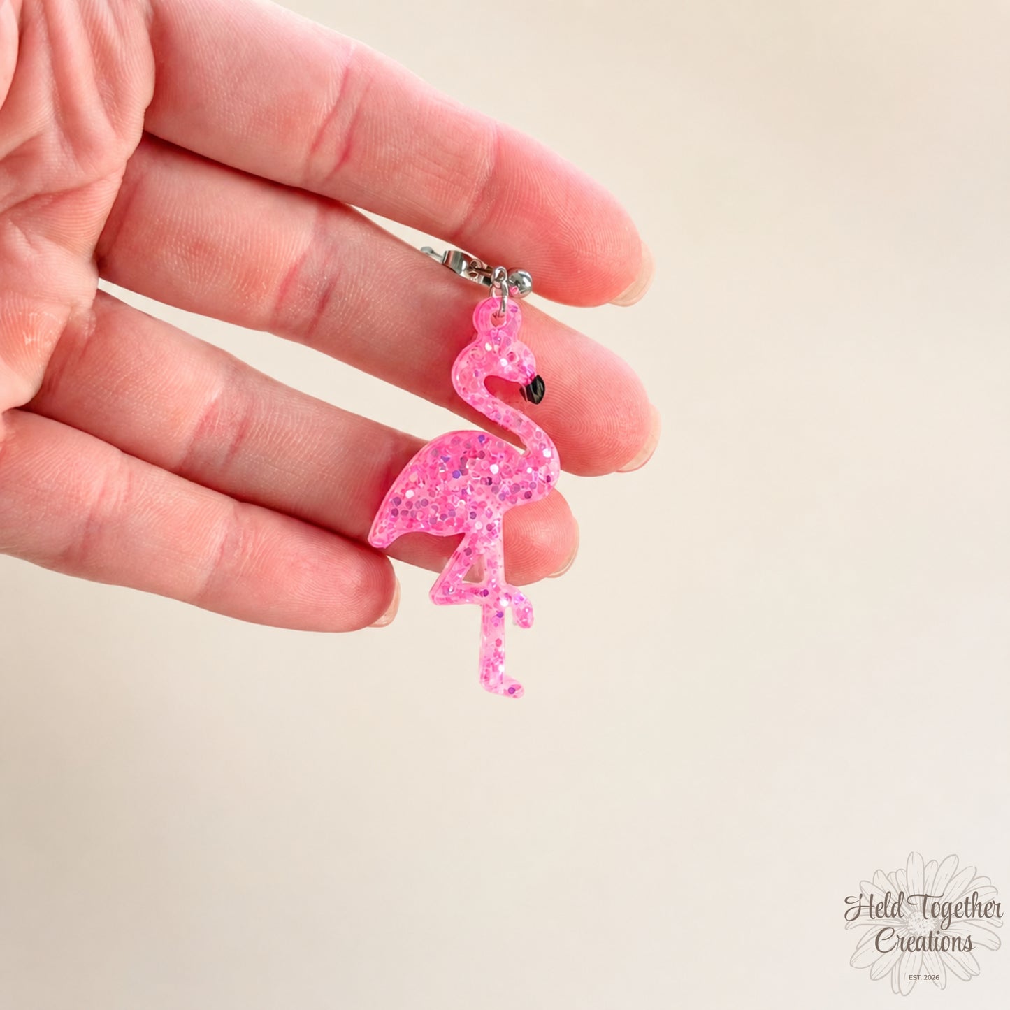 Handmade pink glitter flamingo resin earrings with silver-tone stud hardware on a soft neutral background.