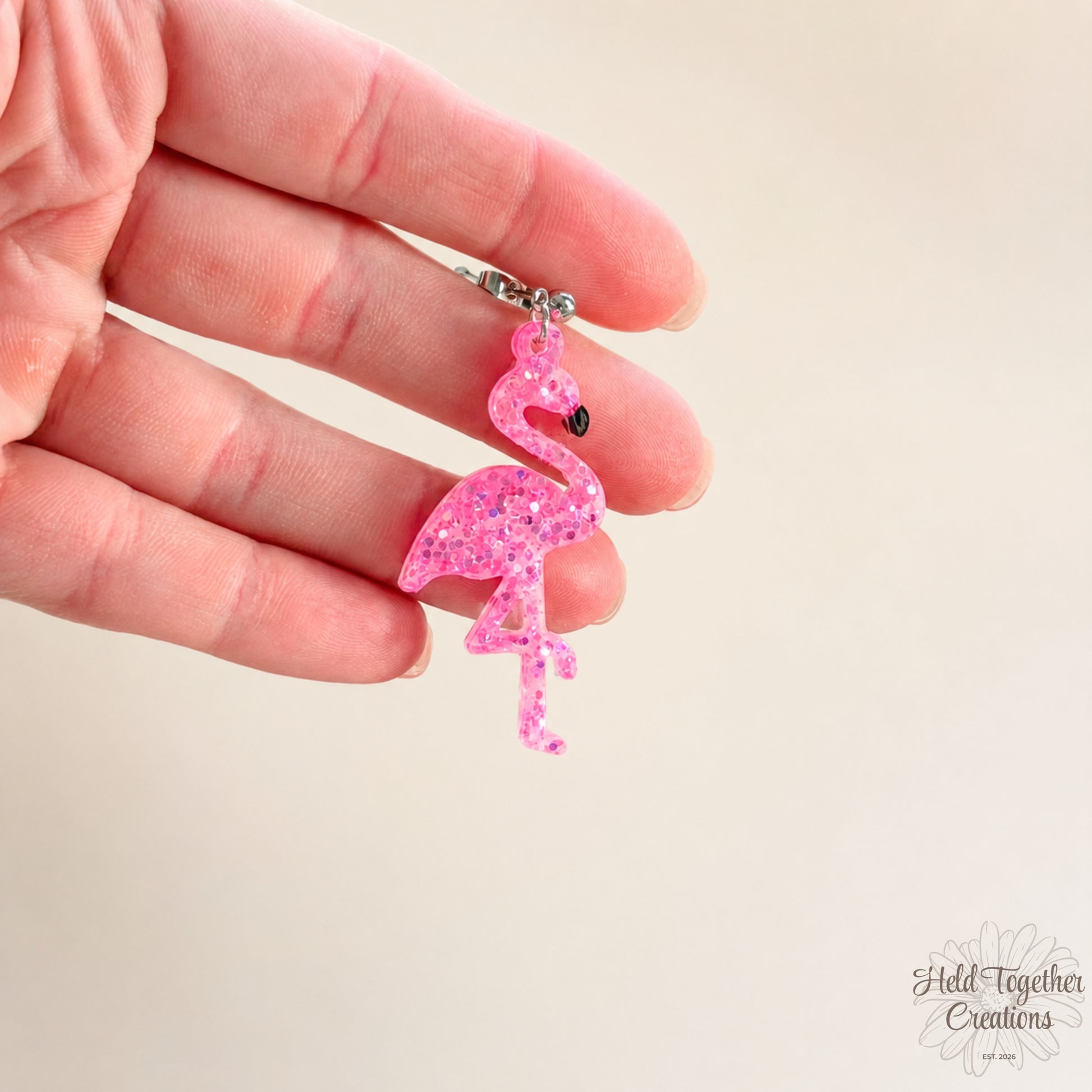 Handmade pink glitter flamingo resin earrings with silver-tone stud hardware on a soft neutral background.
