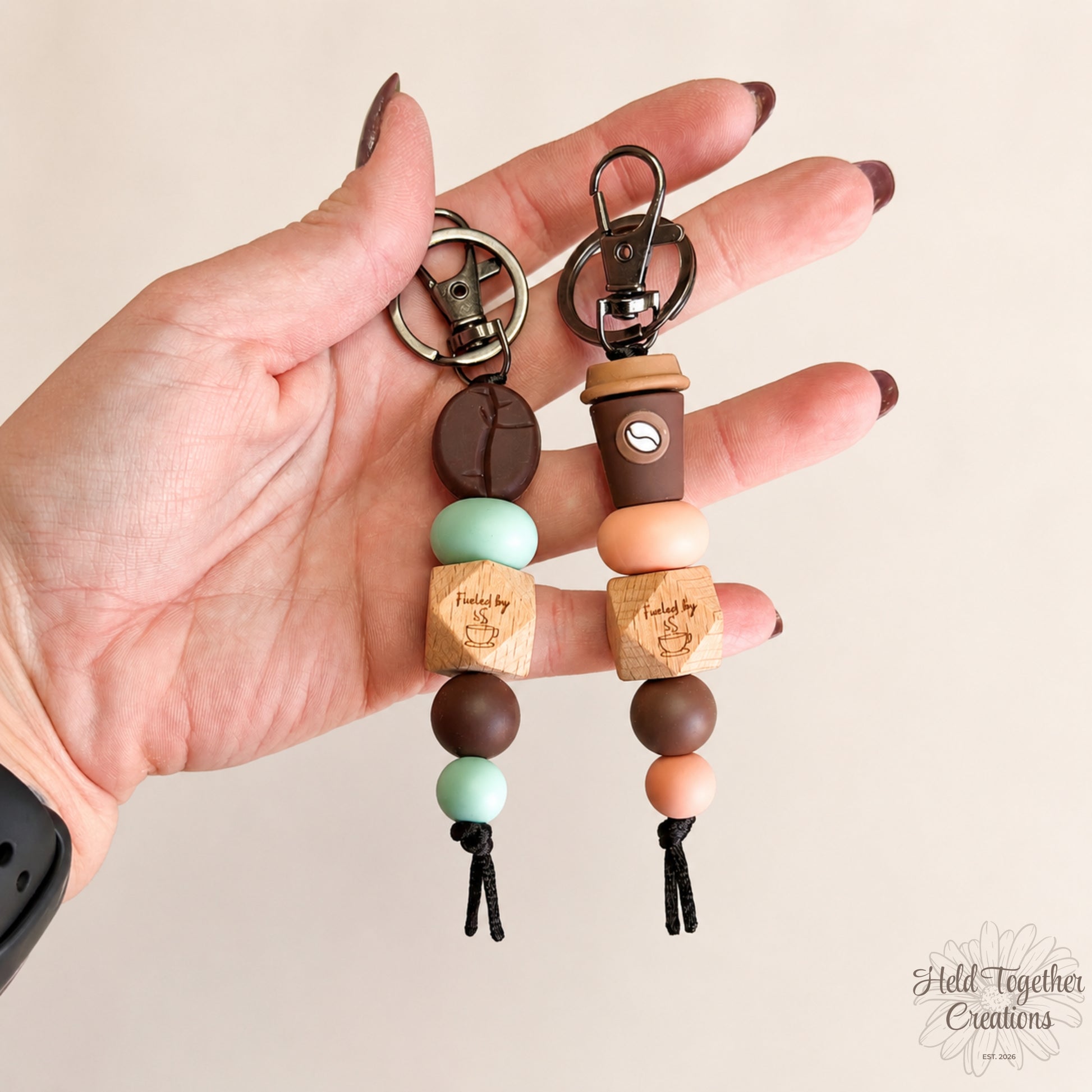 Hand holding two wooden bead keychains with a plain background