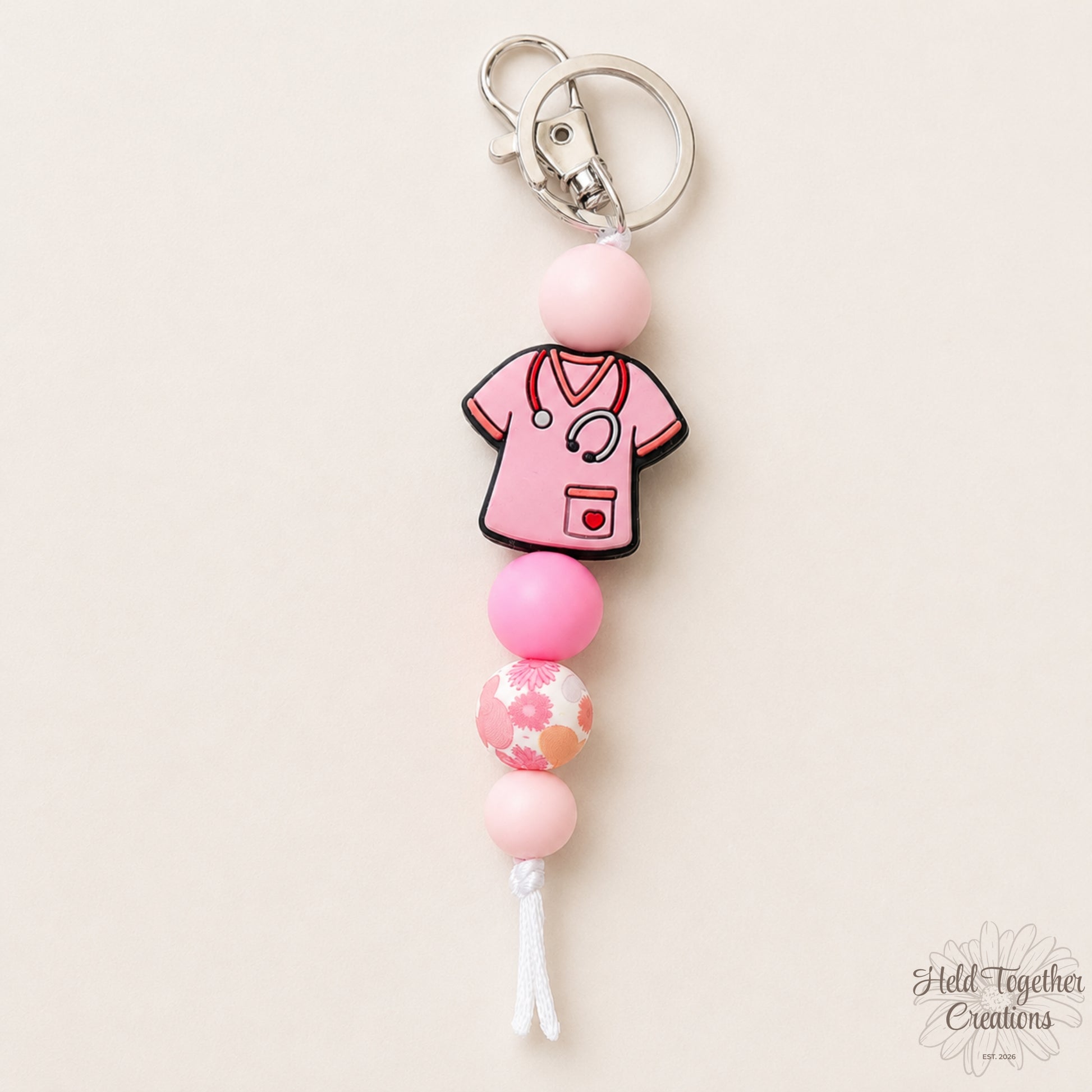 Keychain with pink beaded design and medical scrubs charm on a beige background