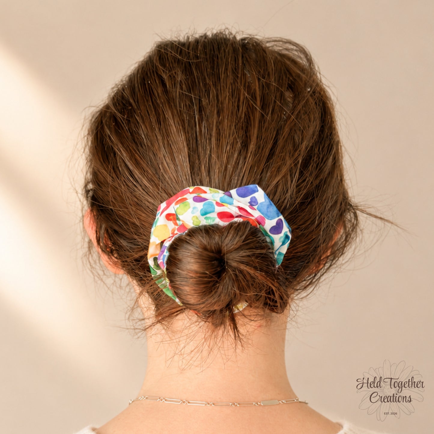 Heart Pop Scrunchie styled in a low bun, showing the colourful heart print against brown hair and a cream knit jumper.