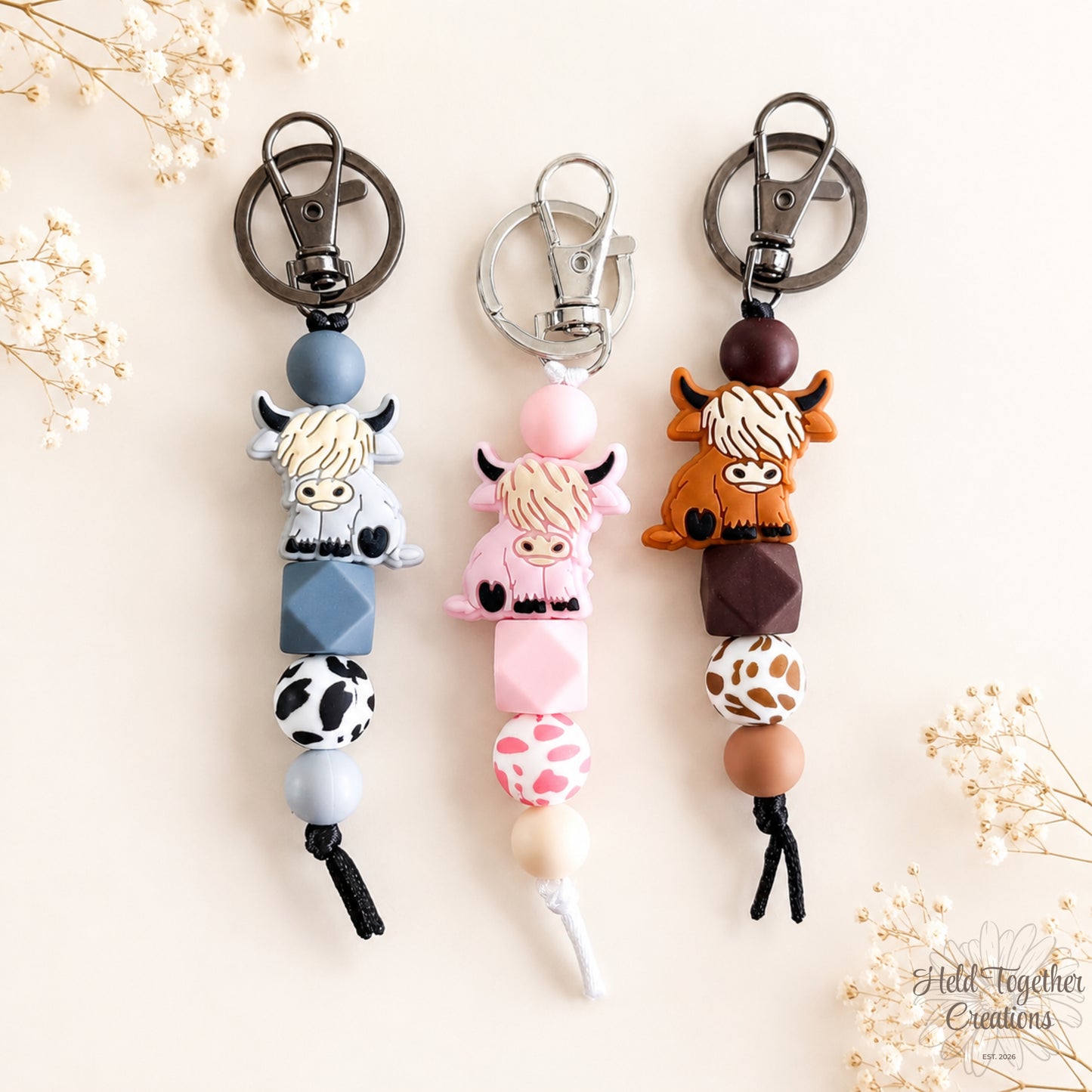 Three cow-themed keychains on a light background with decorative elements.