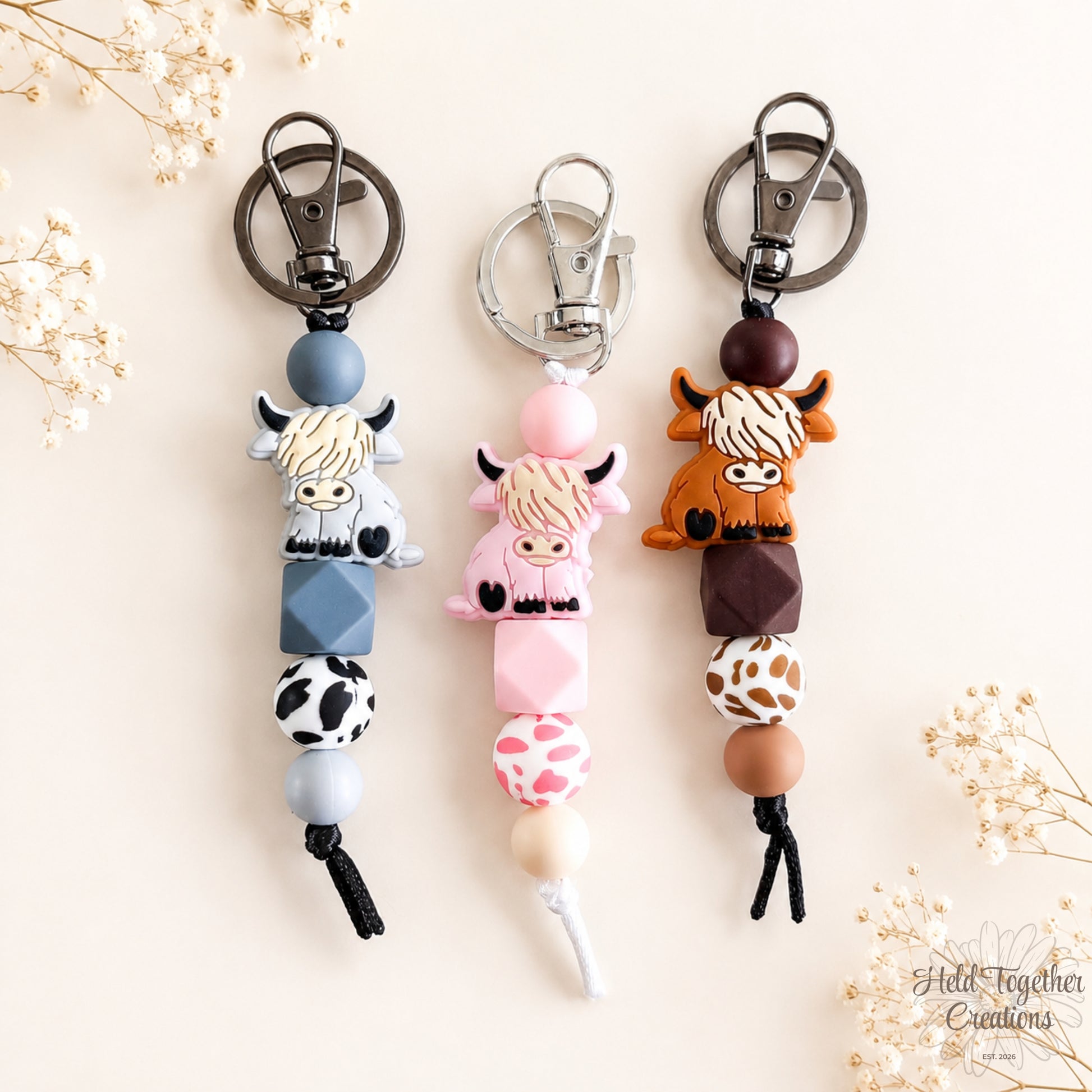 Three cow-themed keychains on a light background with decorative elements.