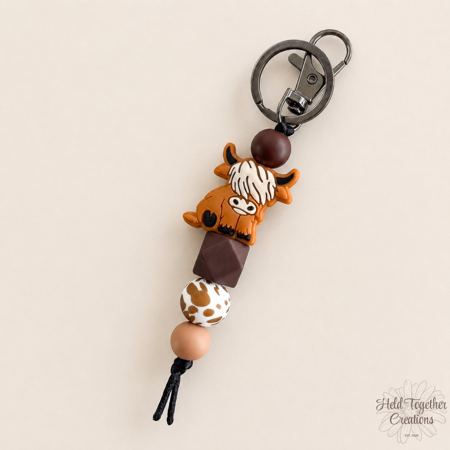 Keychain with cow design and beads on a beige background