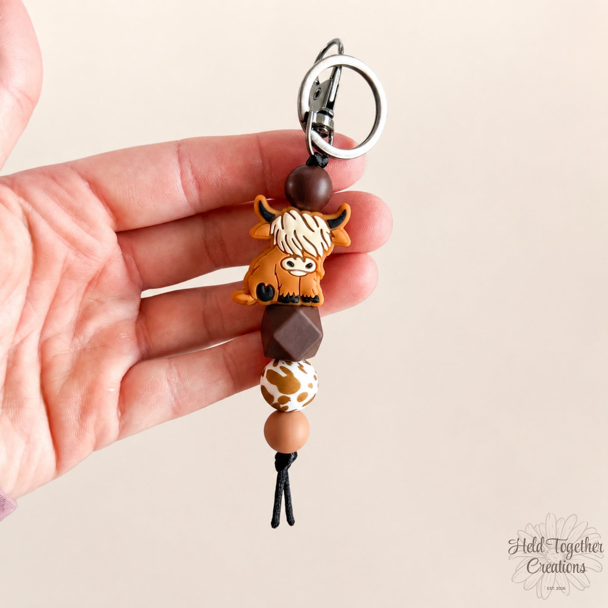 Hand holding a keychain with animal-themed beads on a beige background