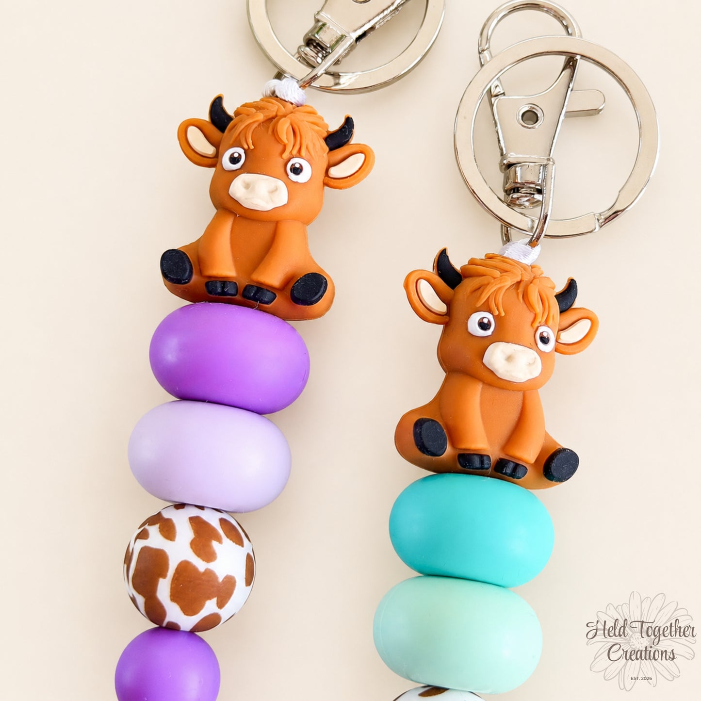 Two cow-shaped keychains with colorful beads on a beige background.
