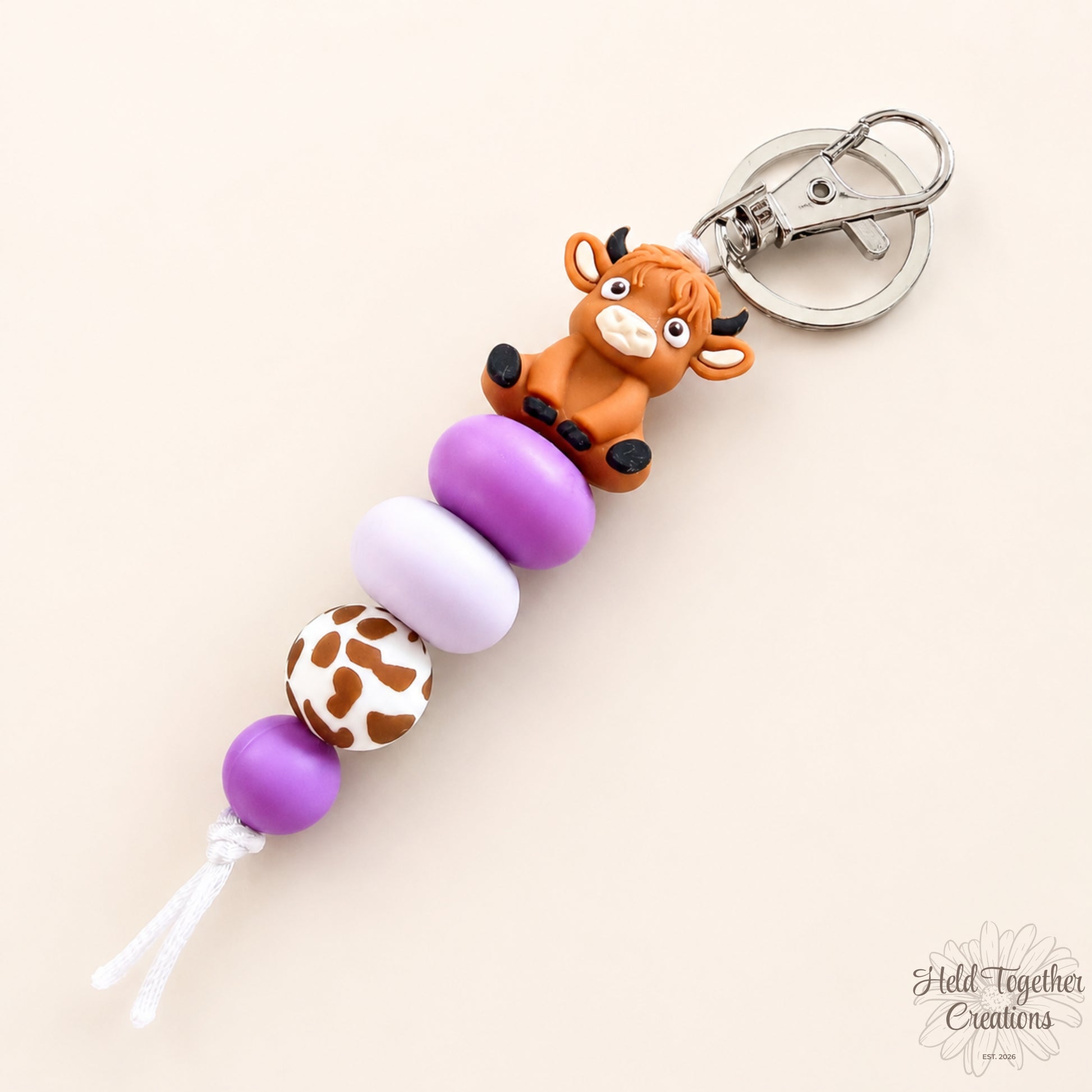 Keychain with purple beads and a cow figurine on a beige background