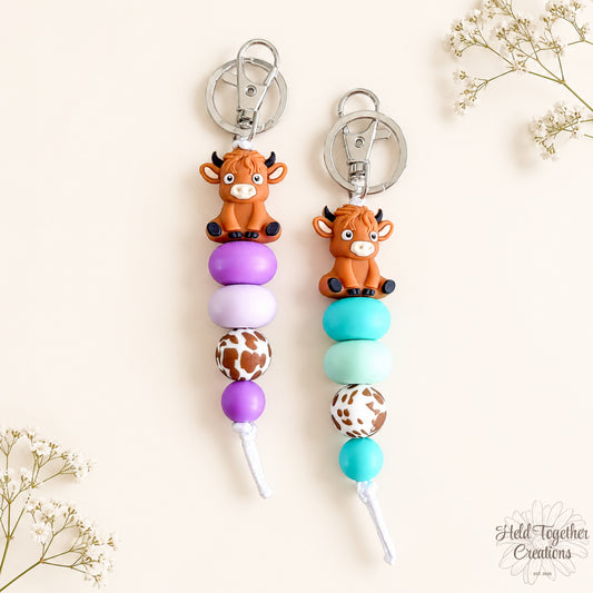 Two keychains with cow charms and colorful beads on a light background.