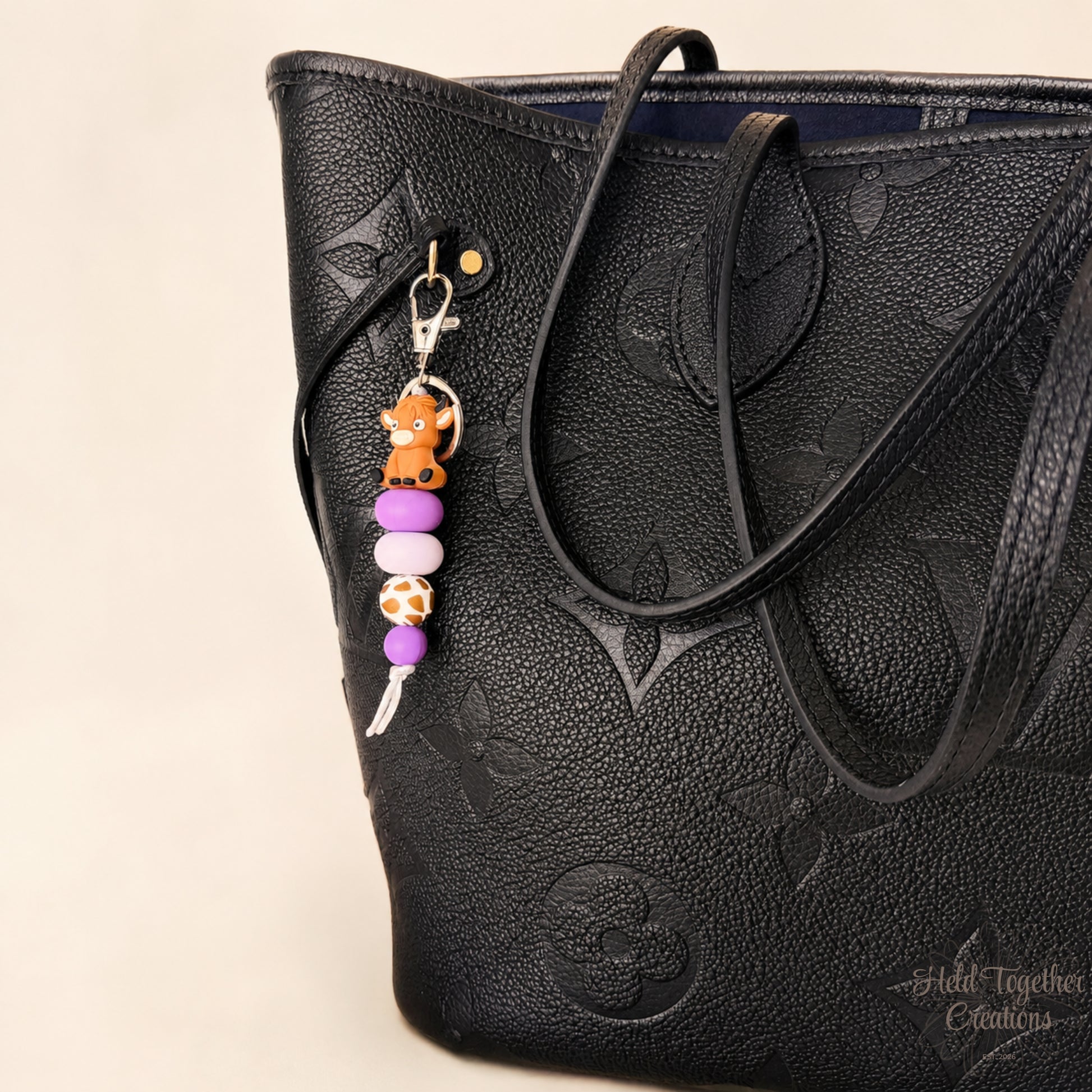 Black textured handbag with a keychain featuring a teddy bear and colorful beads on a beige background.
