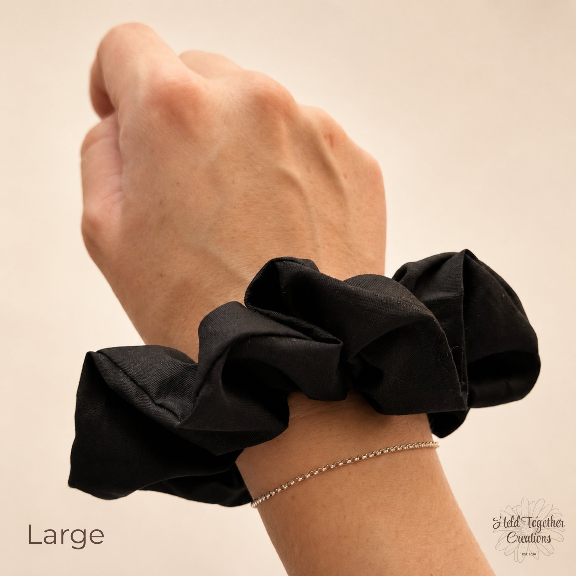 A black fabric hair scrunchie worn on a person's wrist, shown against a plain beige background with the word 'Large' in the lower left corner.
