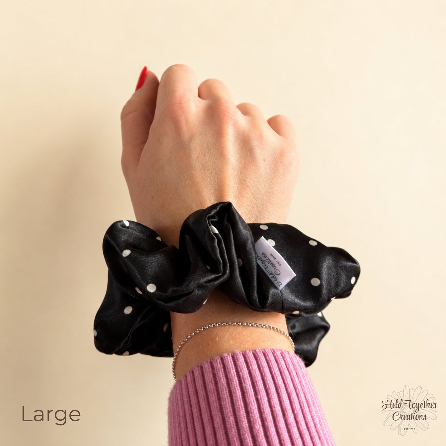 Large black satin scrunchie with white spots worn on the wrist, showing its full gathered style.