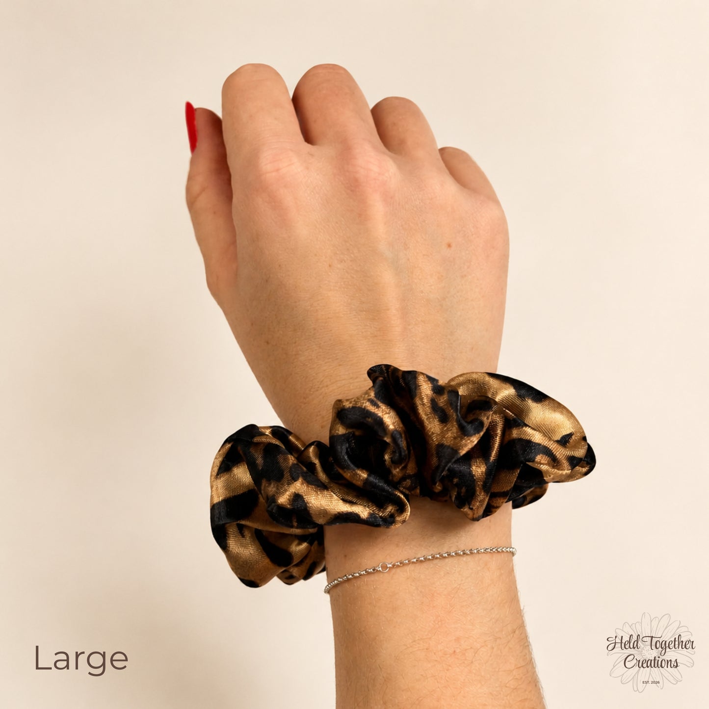 Large leopard satin scrunchie worn on the wrist, showing the size and glossy satin finish.