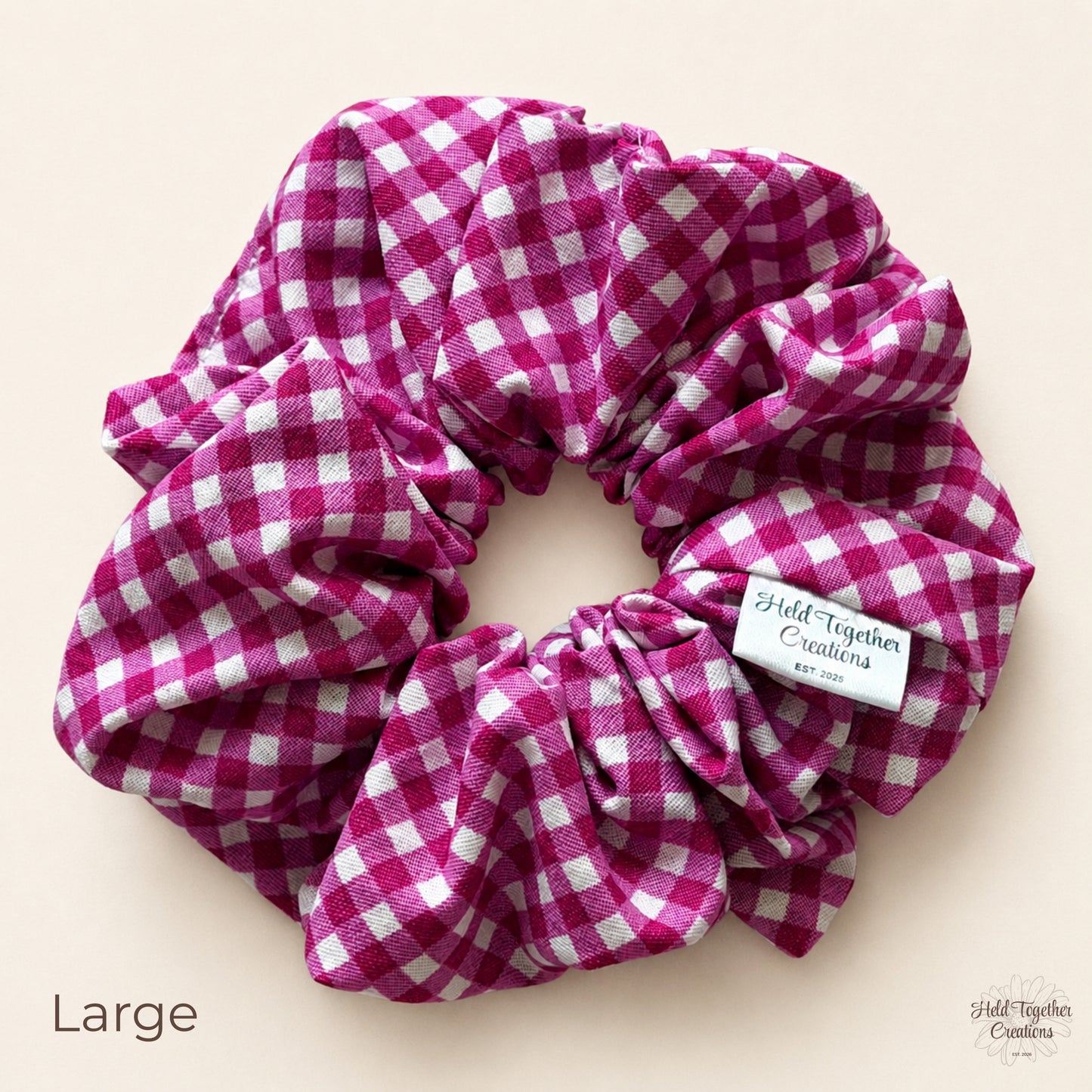 Large mulberry pink and white gingham cotton scrunchie on a warm ivory background.