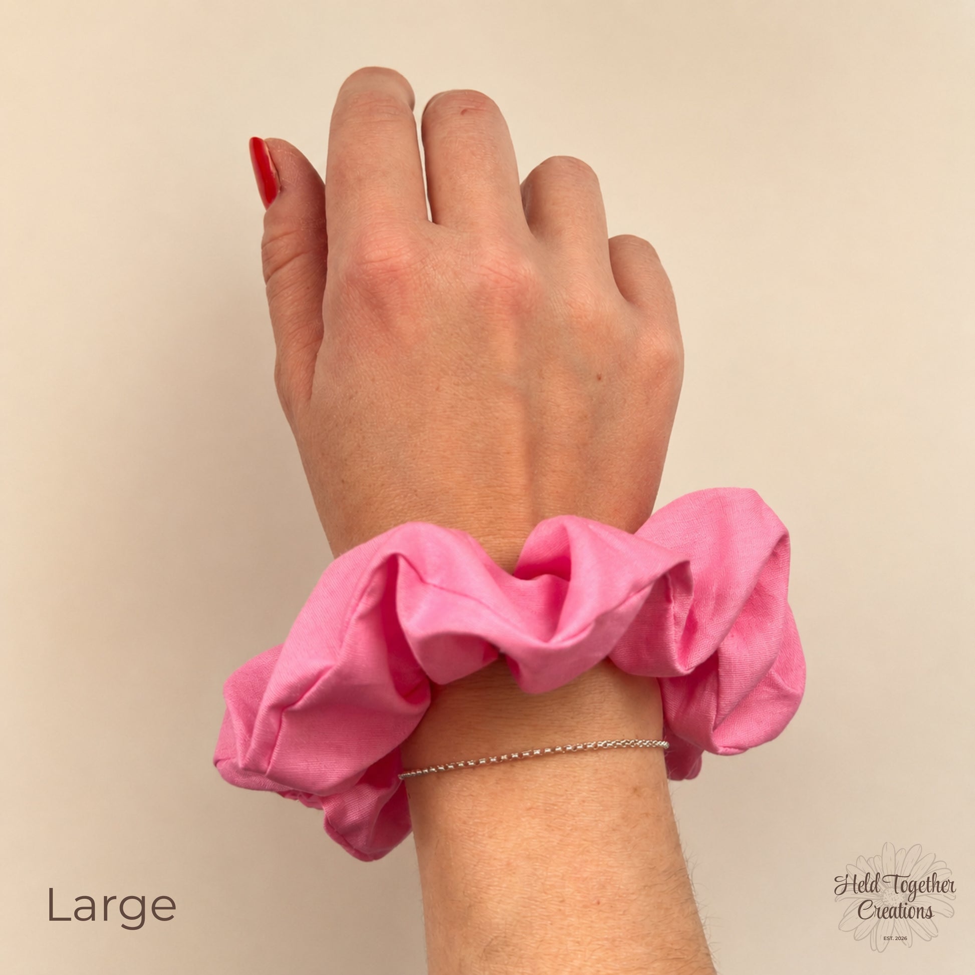 Large pink cotton scrunchie worn on wrist against a neutral background
