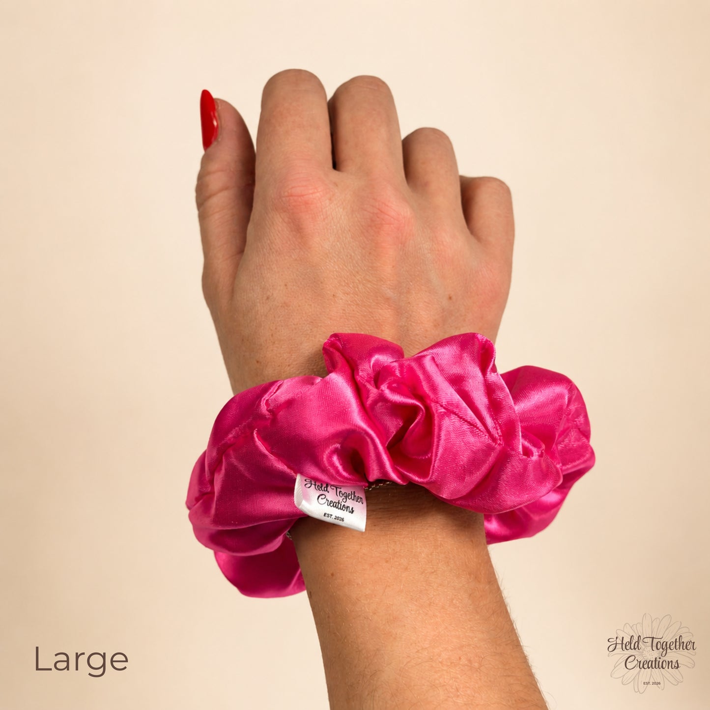 Large pink satin scrunchie worn on wrist against a warm ivory background.