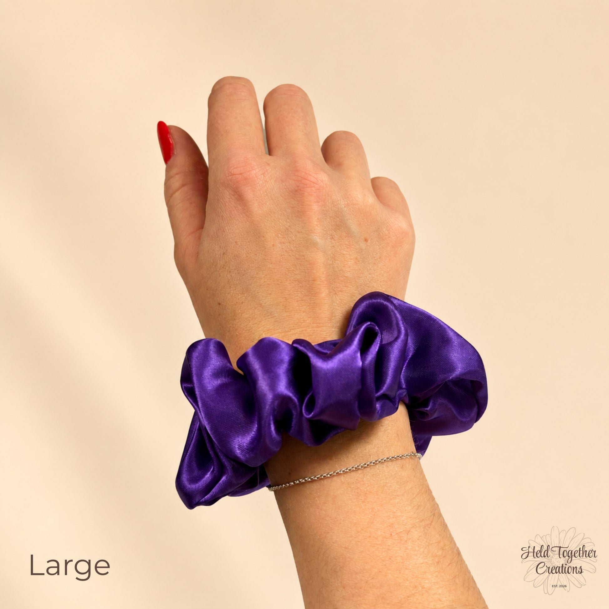 Large purple satin scrunchie worn on a wrist, showing the glossy gathered fabric against a warm ivory background.