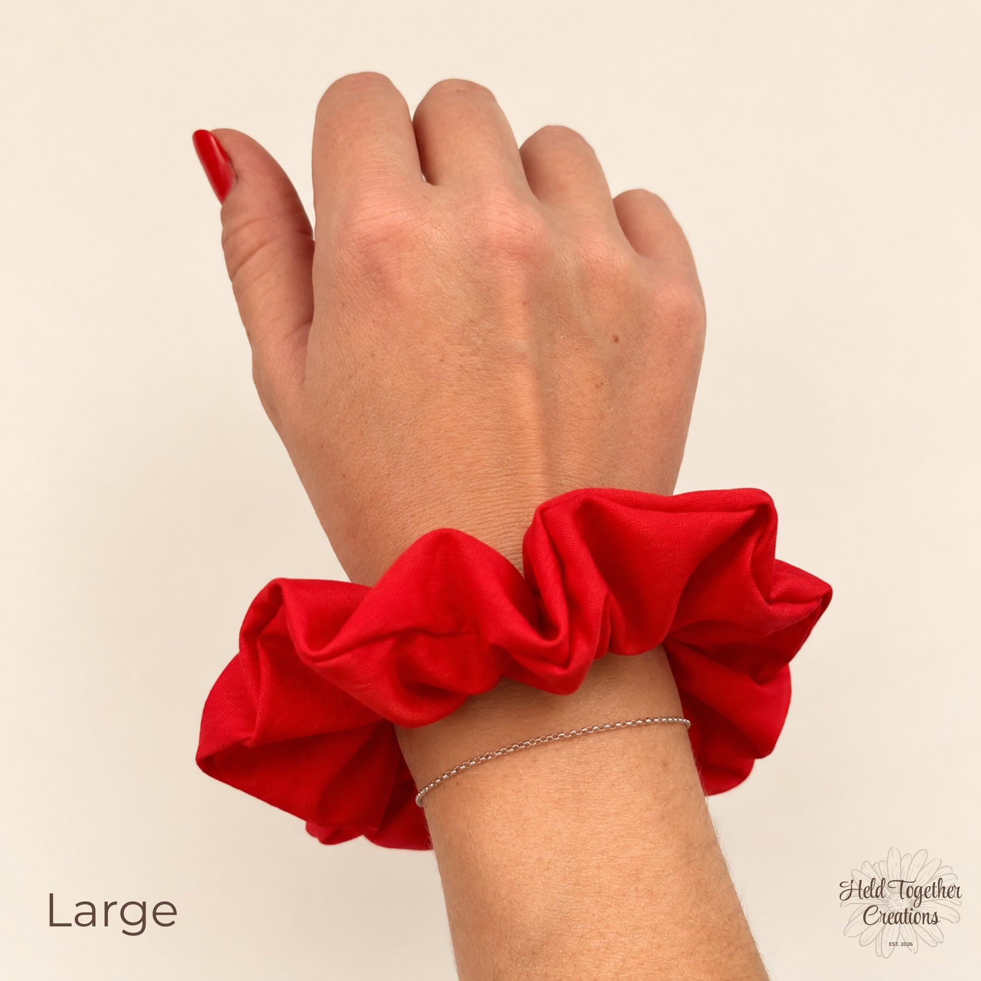 Large red cotton scrunchie worn on wrist against a warm ivory background.