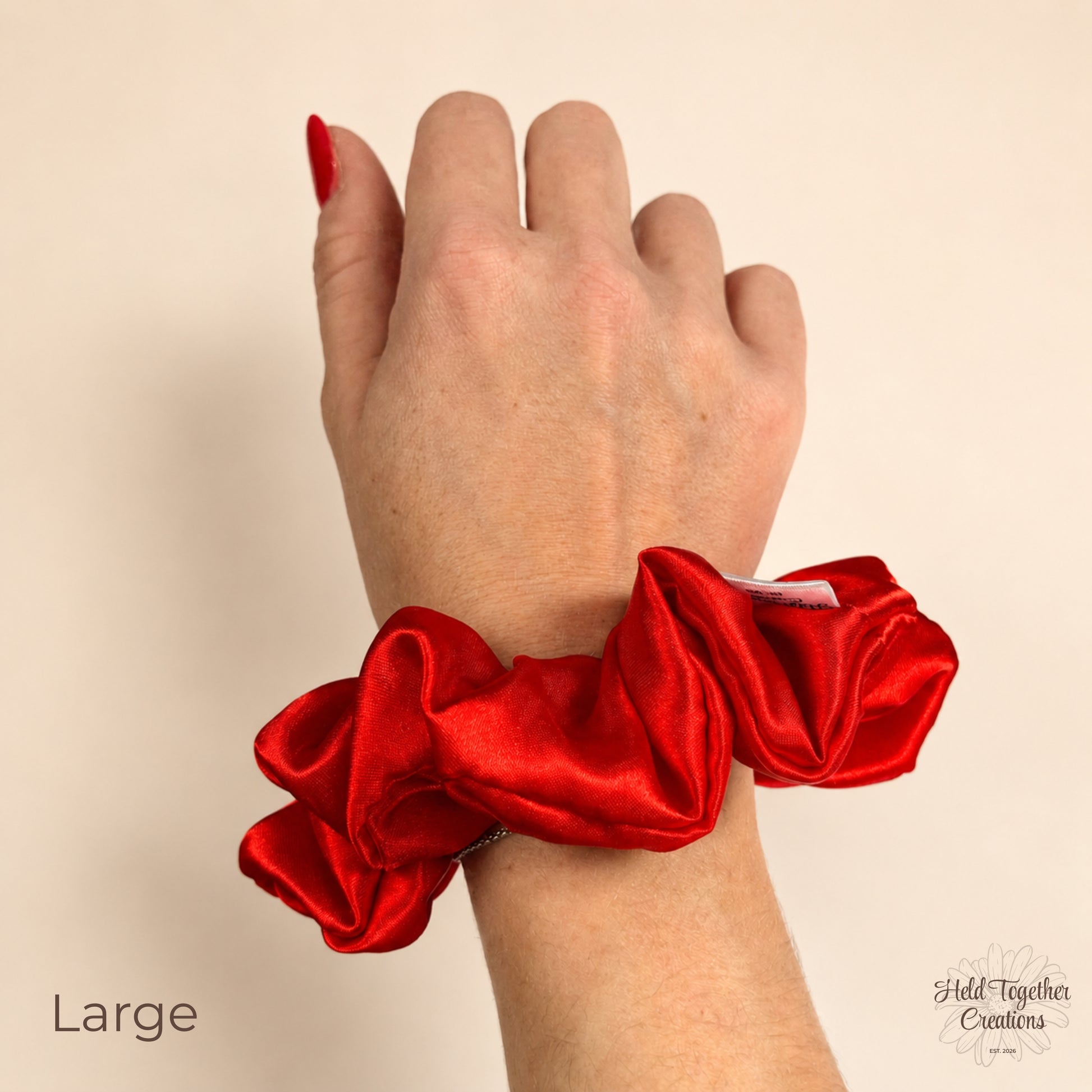 Large red satin scrunchie worn on wrist with glossy gathered fabric