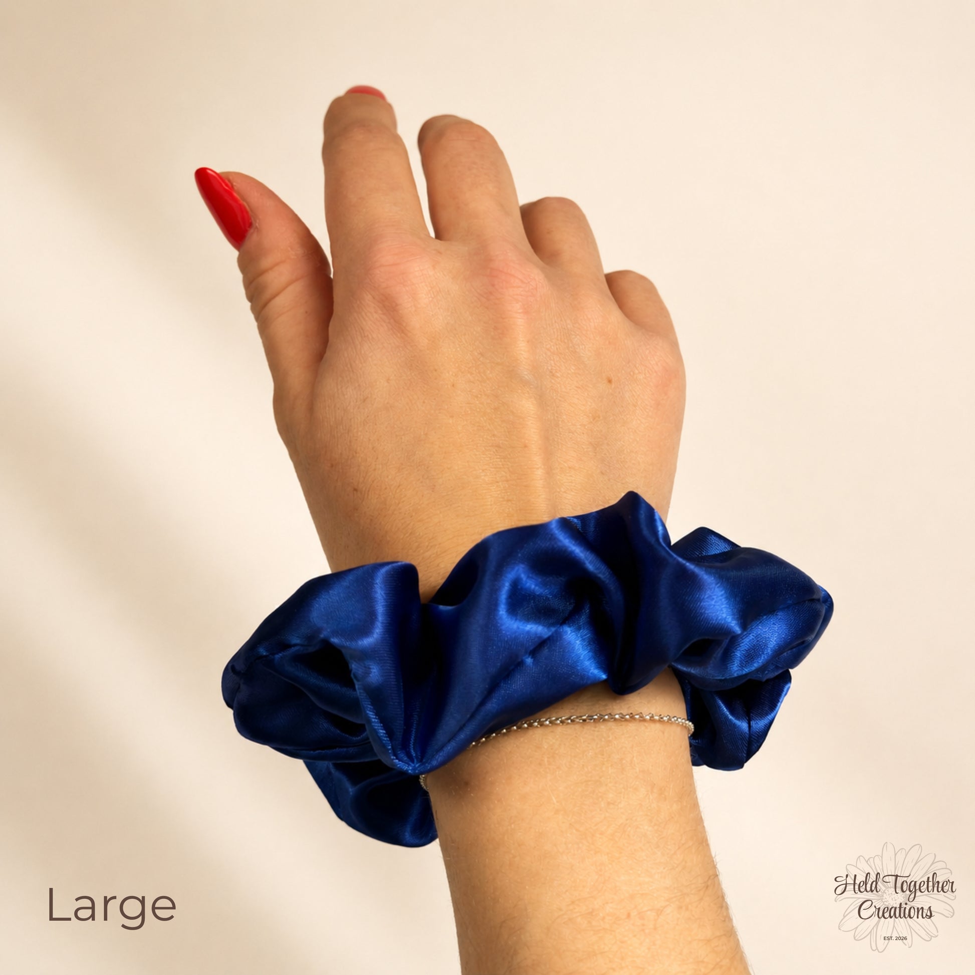 Large royal blue satin scrunchie worn around the wrist on a warm ivory background