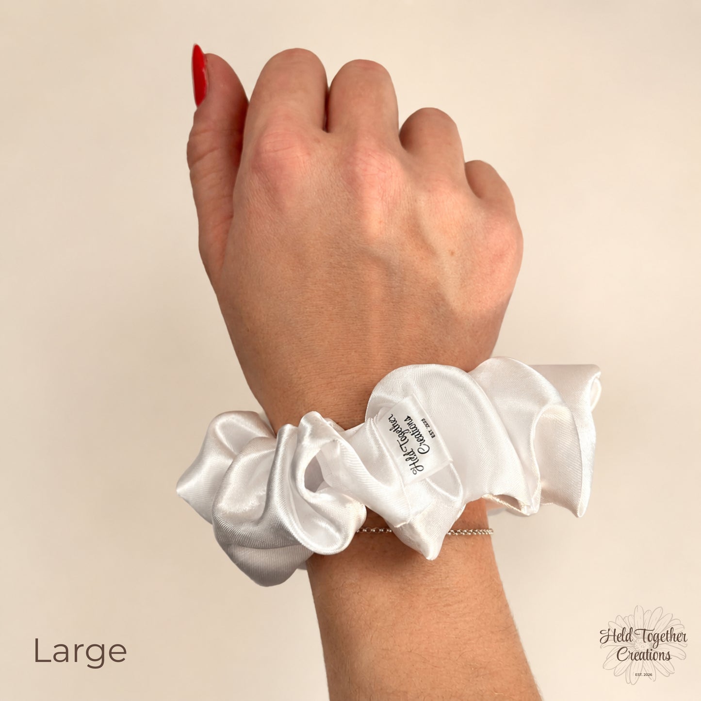 Large white satin scrunchie worn on wrist, showing glossy fabric and soft gathered detail.