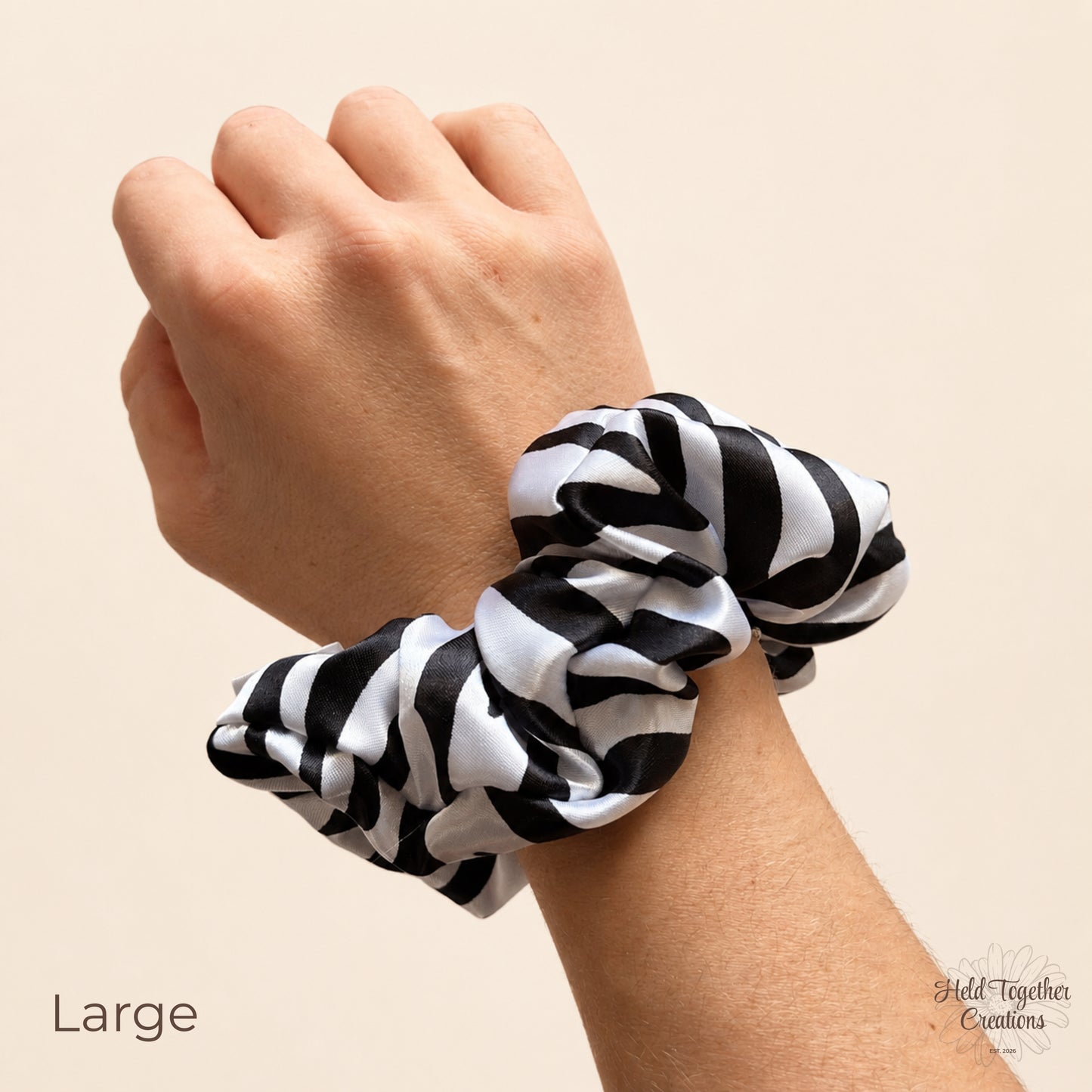 A black and white striped fabric scrunchie worn on a person's wrist, shown against a plain beige background with the word 'Large' in the lower left.