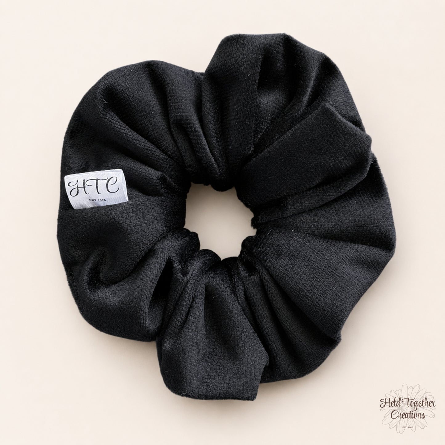Black velvet handmade scrunchie with white HTC label on a warm neutral background.